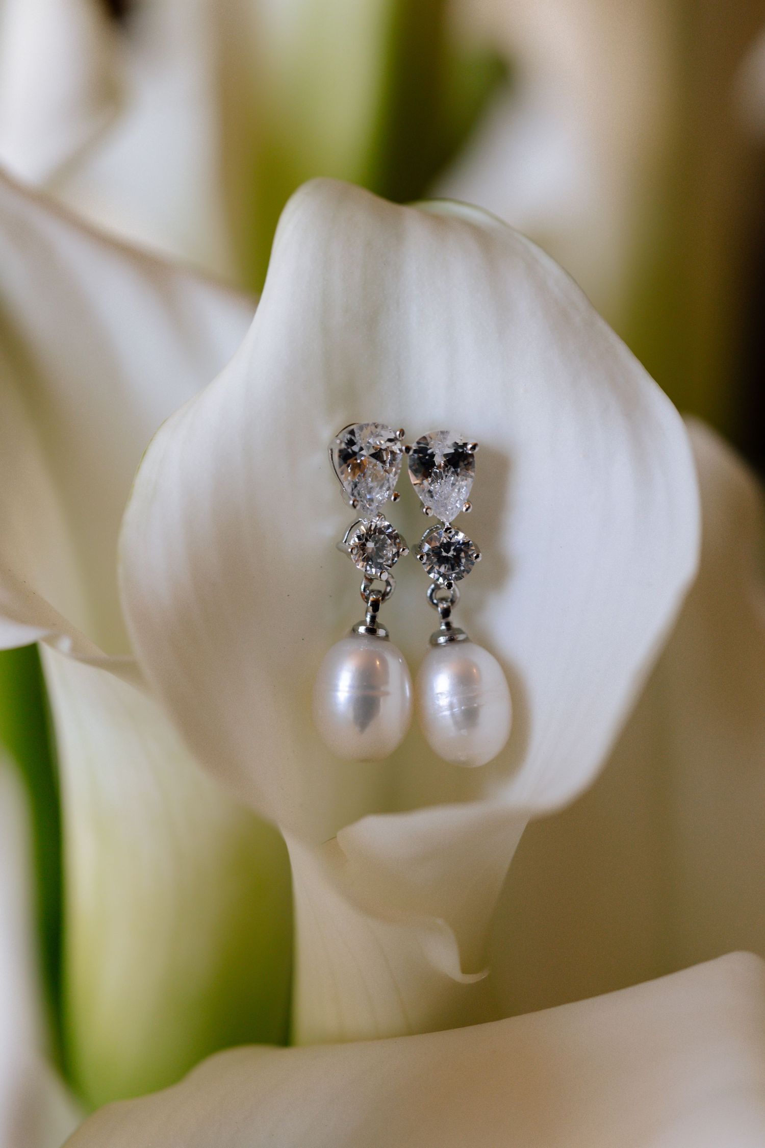 Elegant pearl drop earrings with crystal accents displayed on a white calla lily flower.