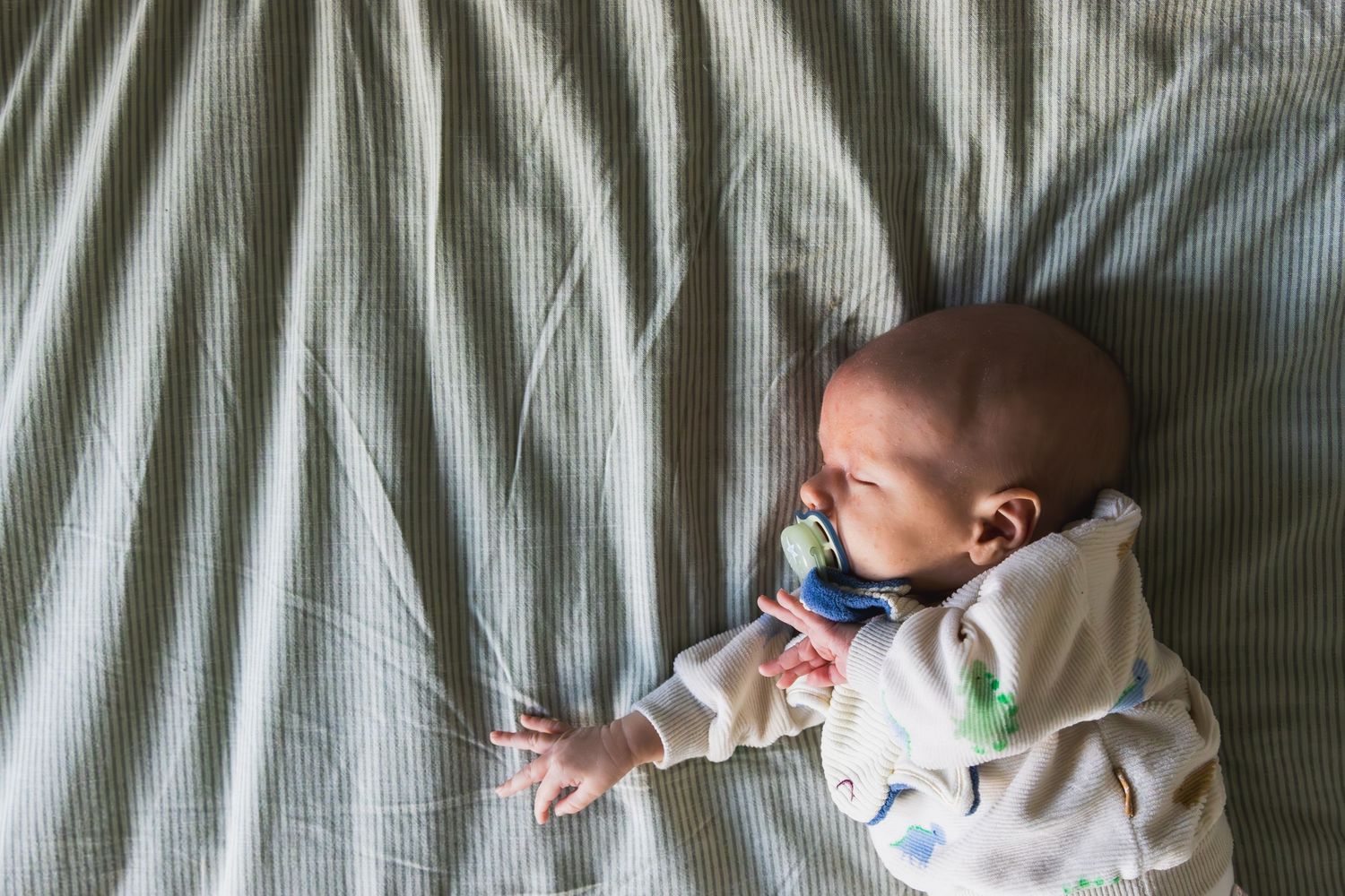 Een pasgeboren baby op een donsdeken. Hij heeft een tutter in zijn mond en steekt zijn armen voor zich uit