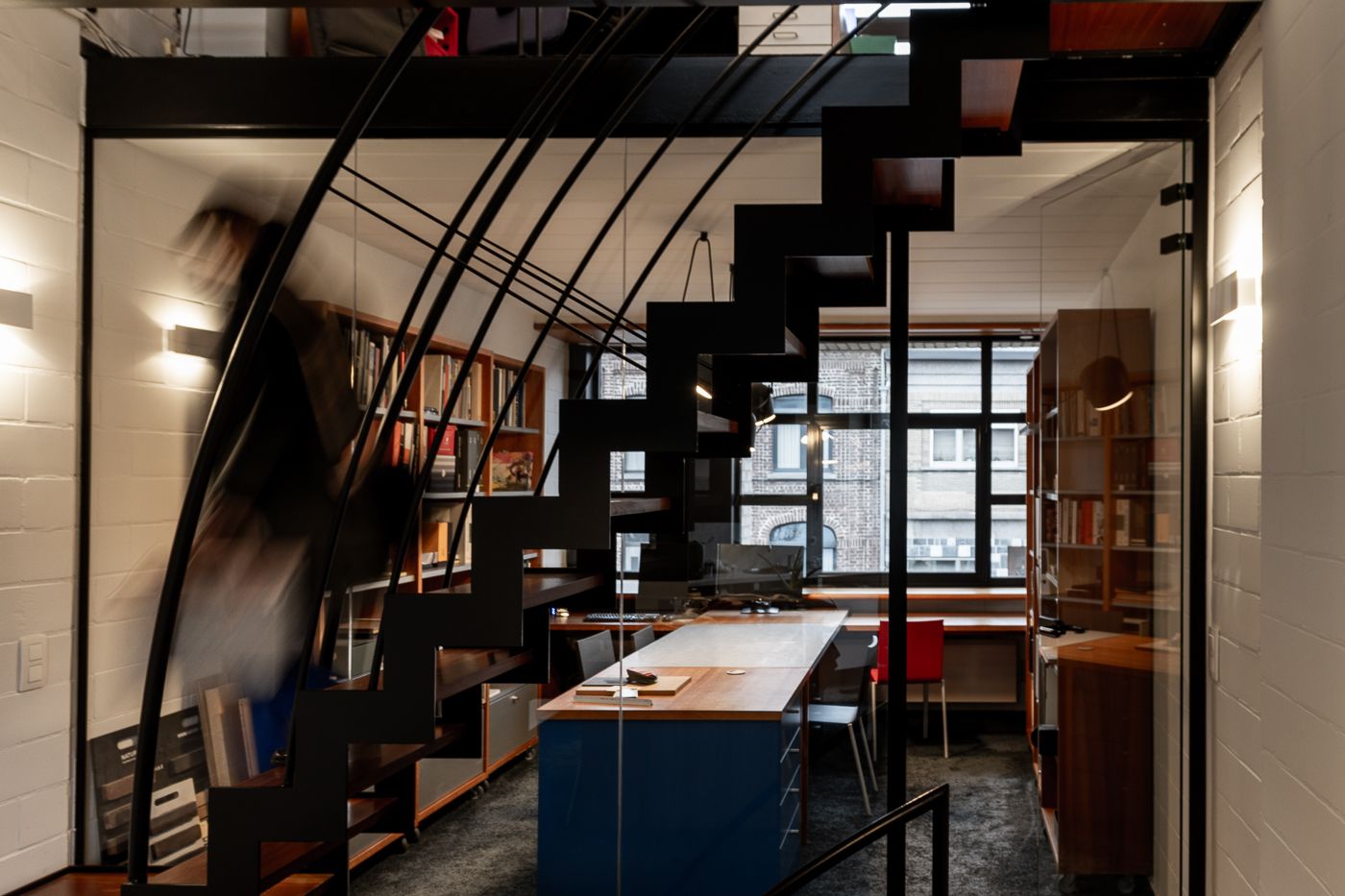 Een binnenruimte van een architectenbureau. De trap loopt schuin door de foto, terwijl er een bewegende schim de trap afgaat.