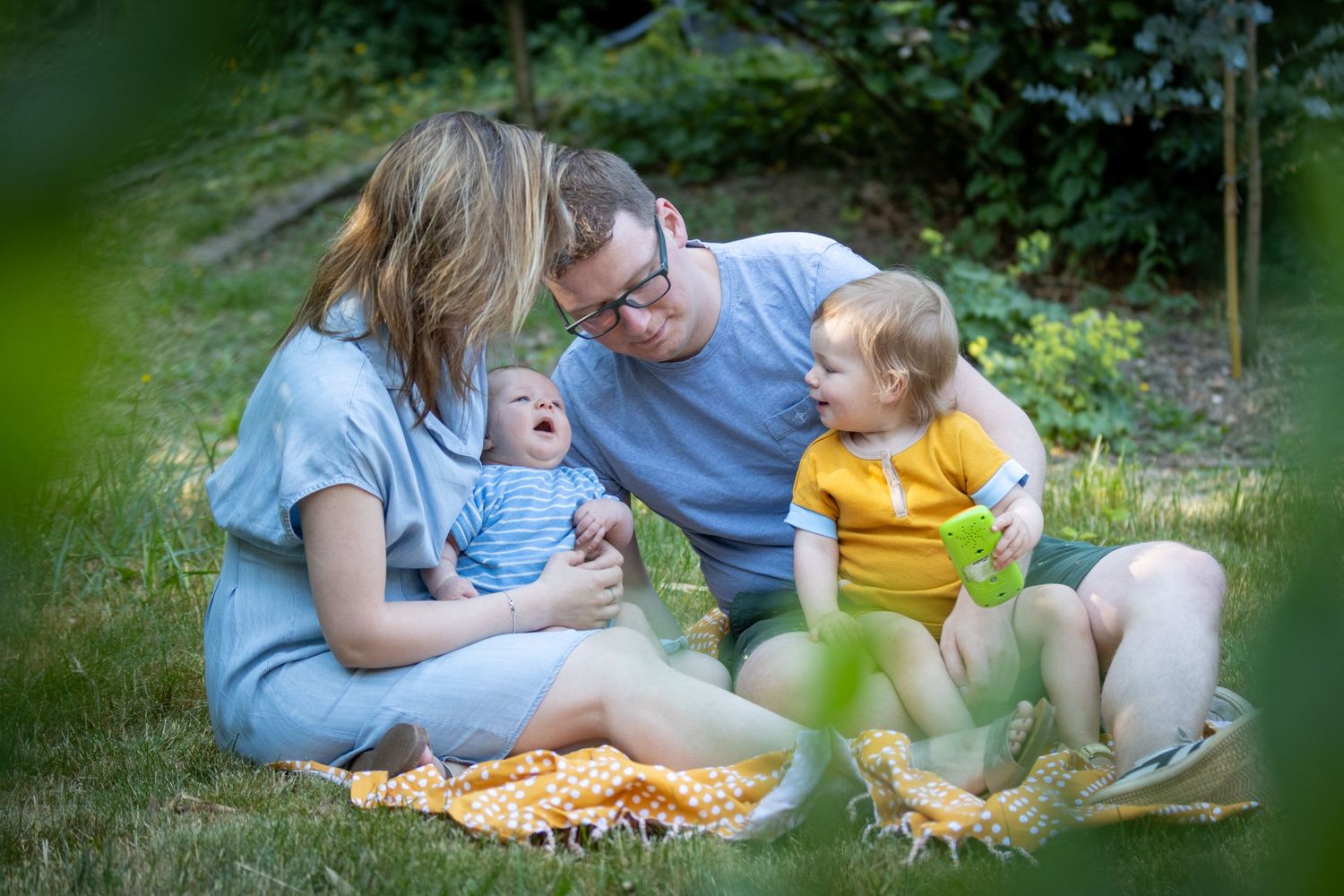 Een portret van een gezin. Pape blauw t-shirt, mama blauw kleed, tweejarige dochter met geel kleed en baby zoontje  met blauw t-shirt.