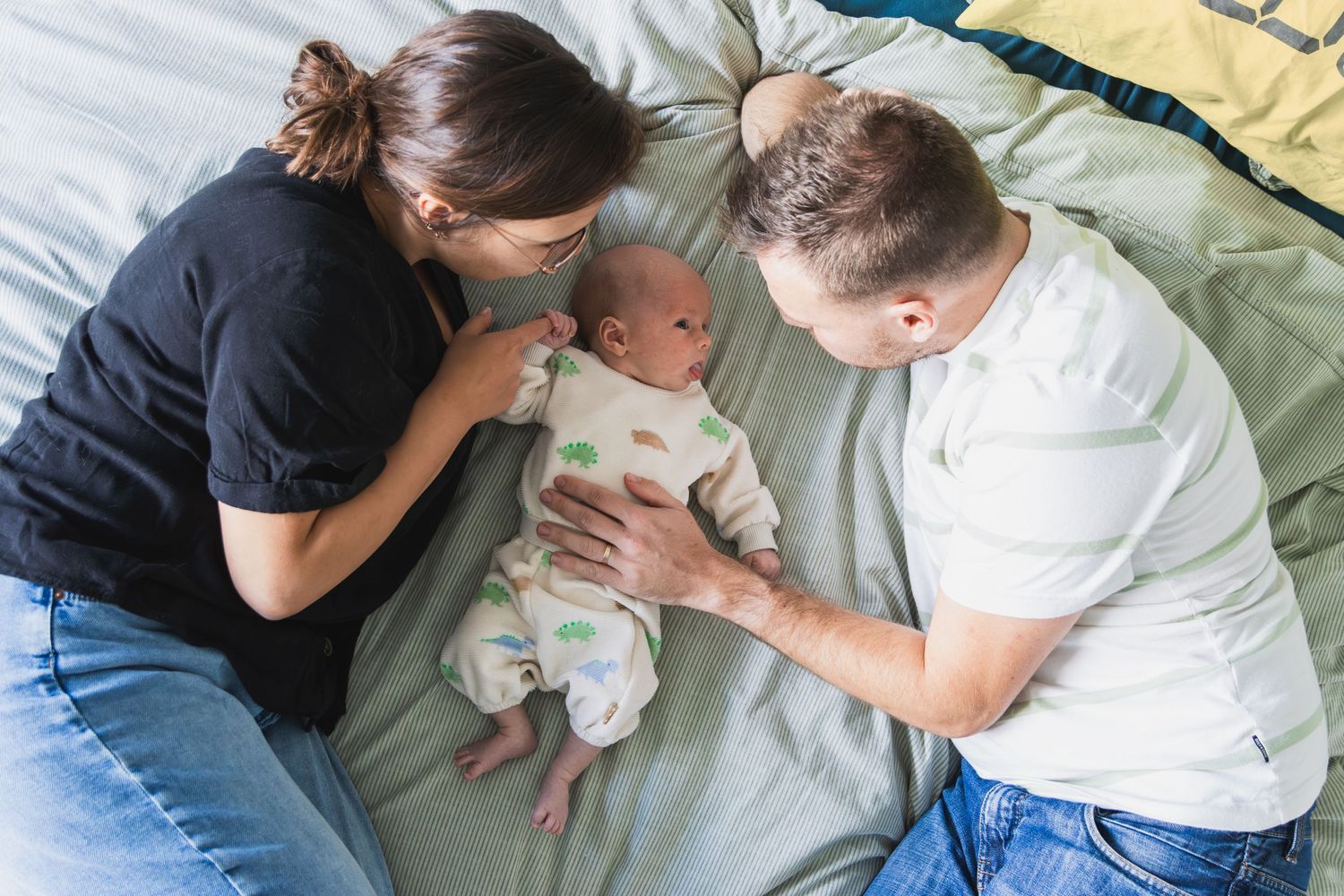 Een familieportret. een vrouw en man liggen op hun zij op bed met hun pasgeboren baby tussen hen in.