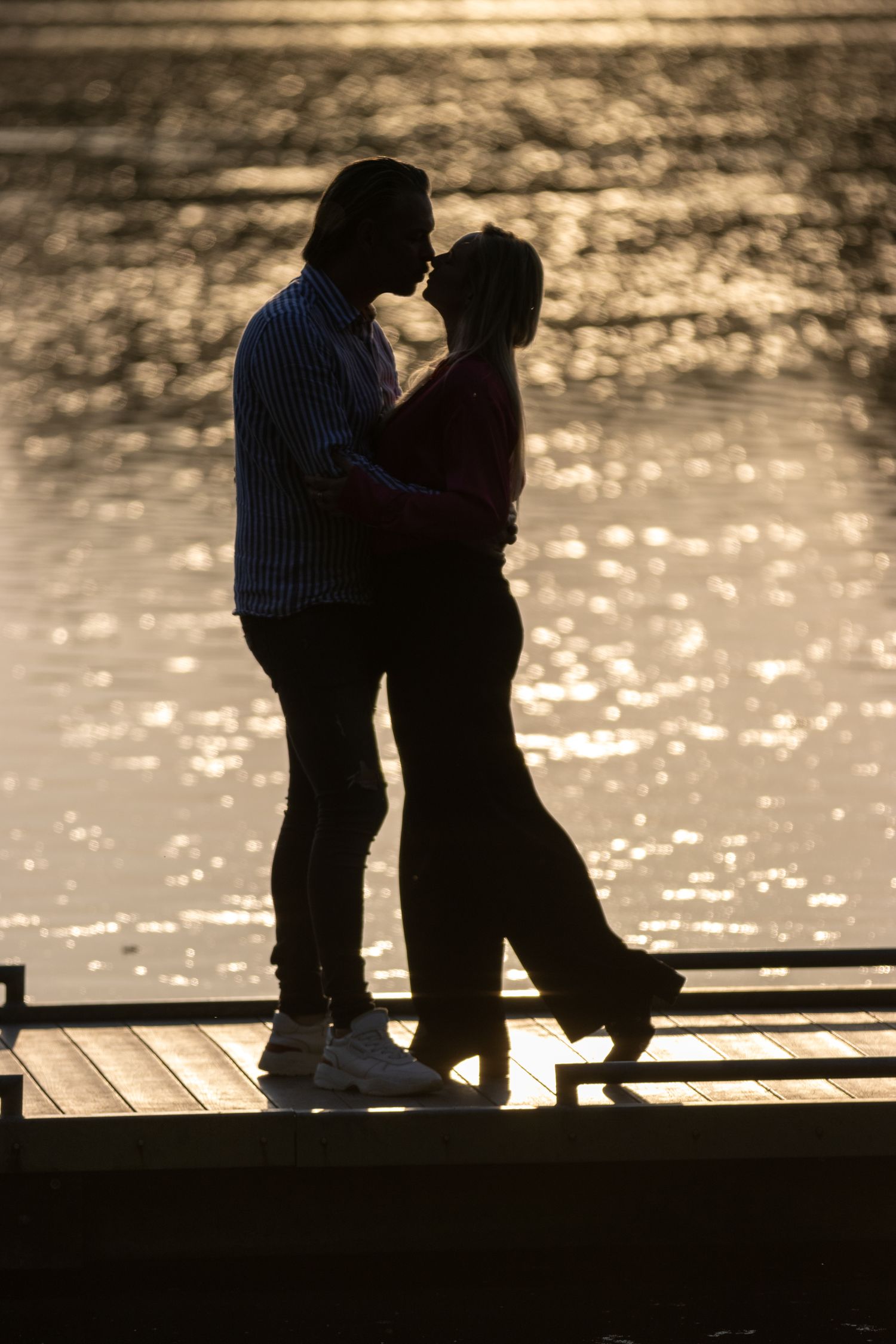 Een silhouet van een verliefd koppel. Ze zijn een man en vrouw die kussen. op de achtergrond water met de zon weerspiegeld.