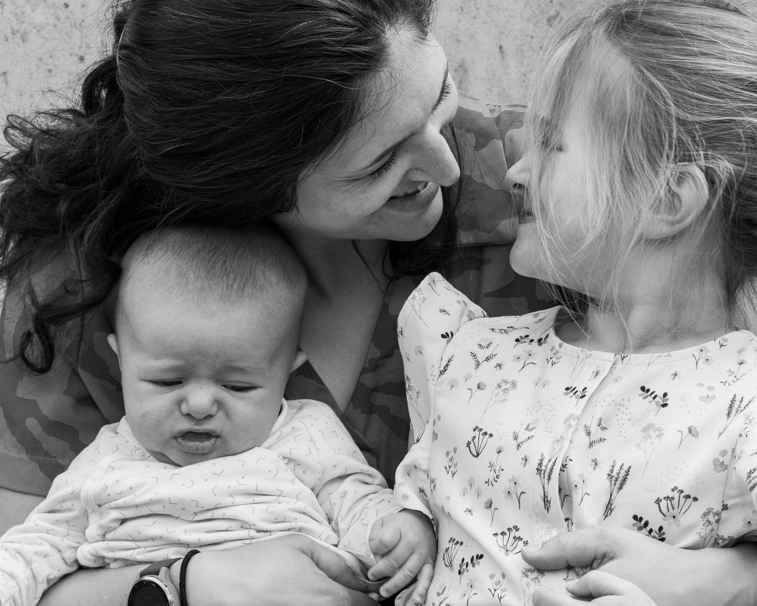 Een zwart-wit gezinsfoto van een vrouw met lange zwarte haren en haar dochter van 4 jaar en baby. De dochter en moeder kijken naar elkaar