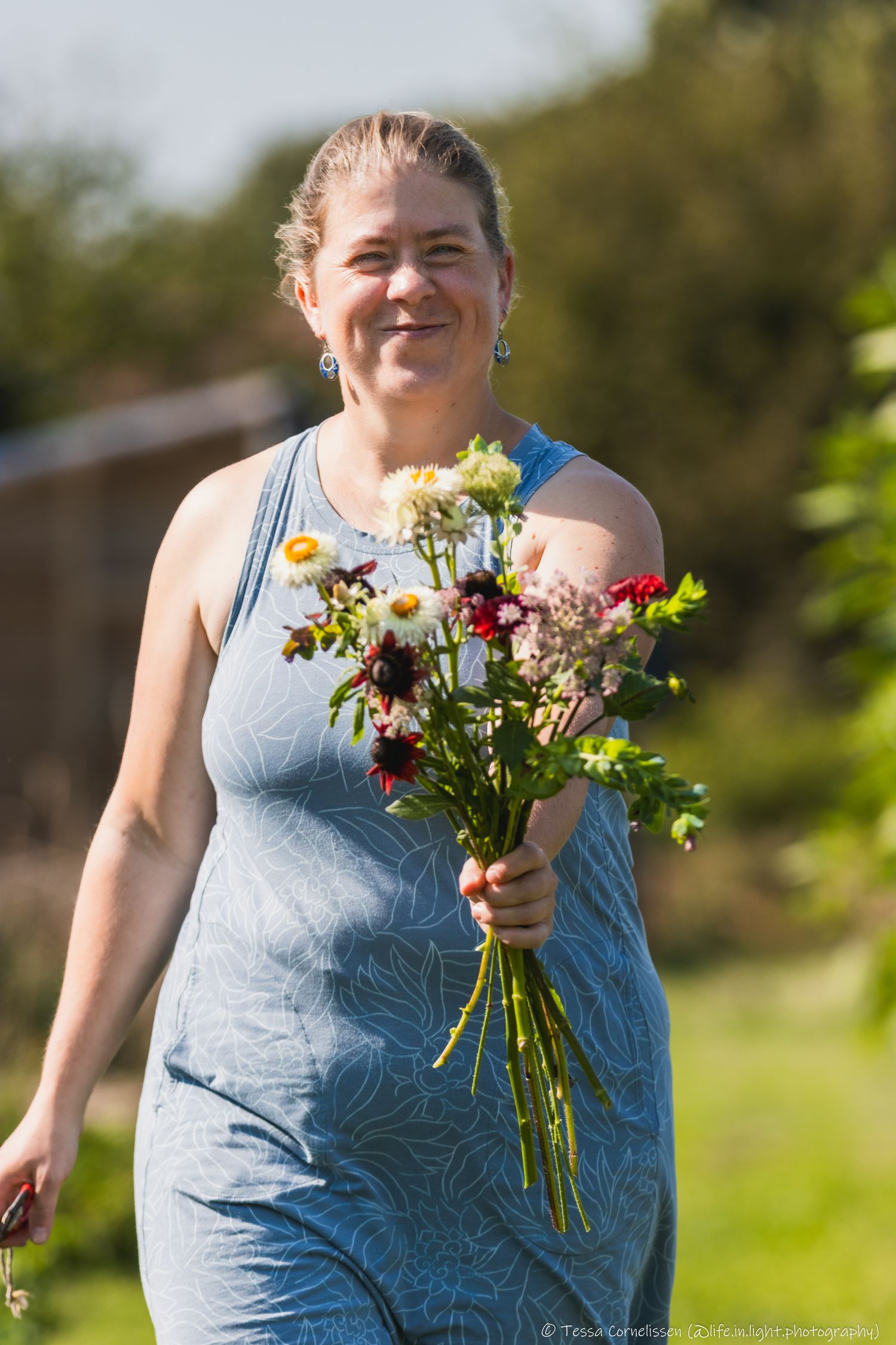 Een vrouw met een blauw kleed komt aangelopen terwijl ze een boeket met vers geplukte bloemen voor haar houdt.