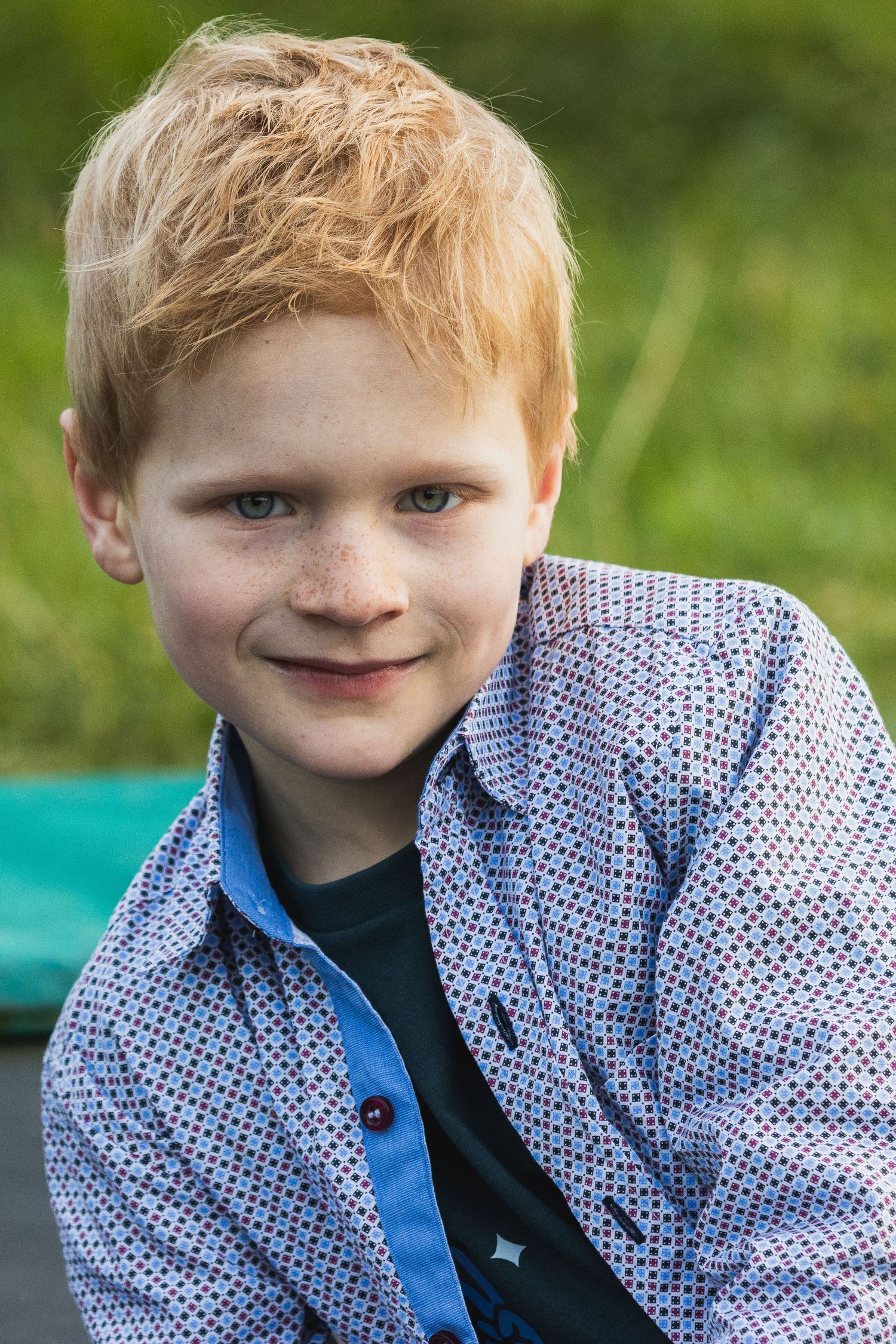 Een portret van een jongen van 10 jaar met ros haar. HIj glimlacht en kijkt recht in de lens. Hij heeft een blauw hemd aan.