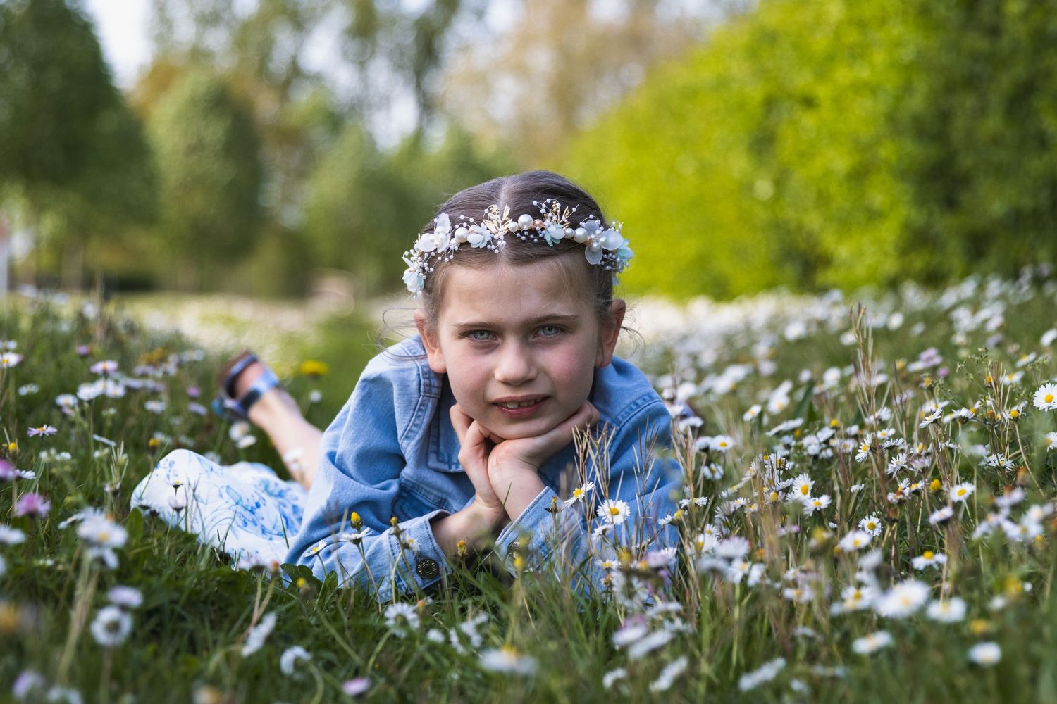 een communiefoto van een zesjarig meisje. Ze ligt op haar buik in het gras tussen de madeliefjes. Bloemen in haar haar.