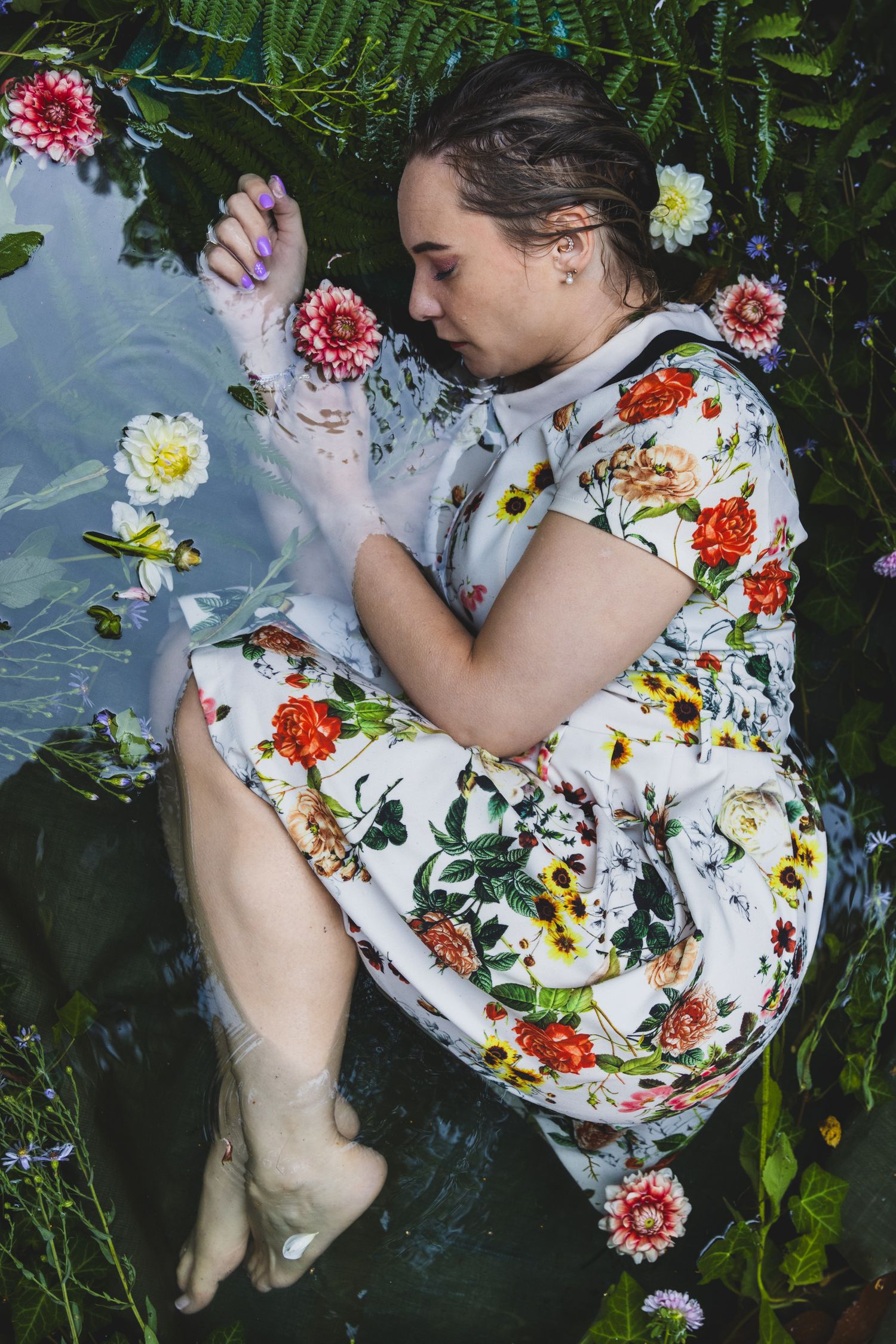 Een portret van een vrouw met doordringende blauwe ogen met een gebloemde jurk in het water omringd met roze bloemen. Ophelia stijl