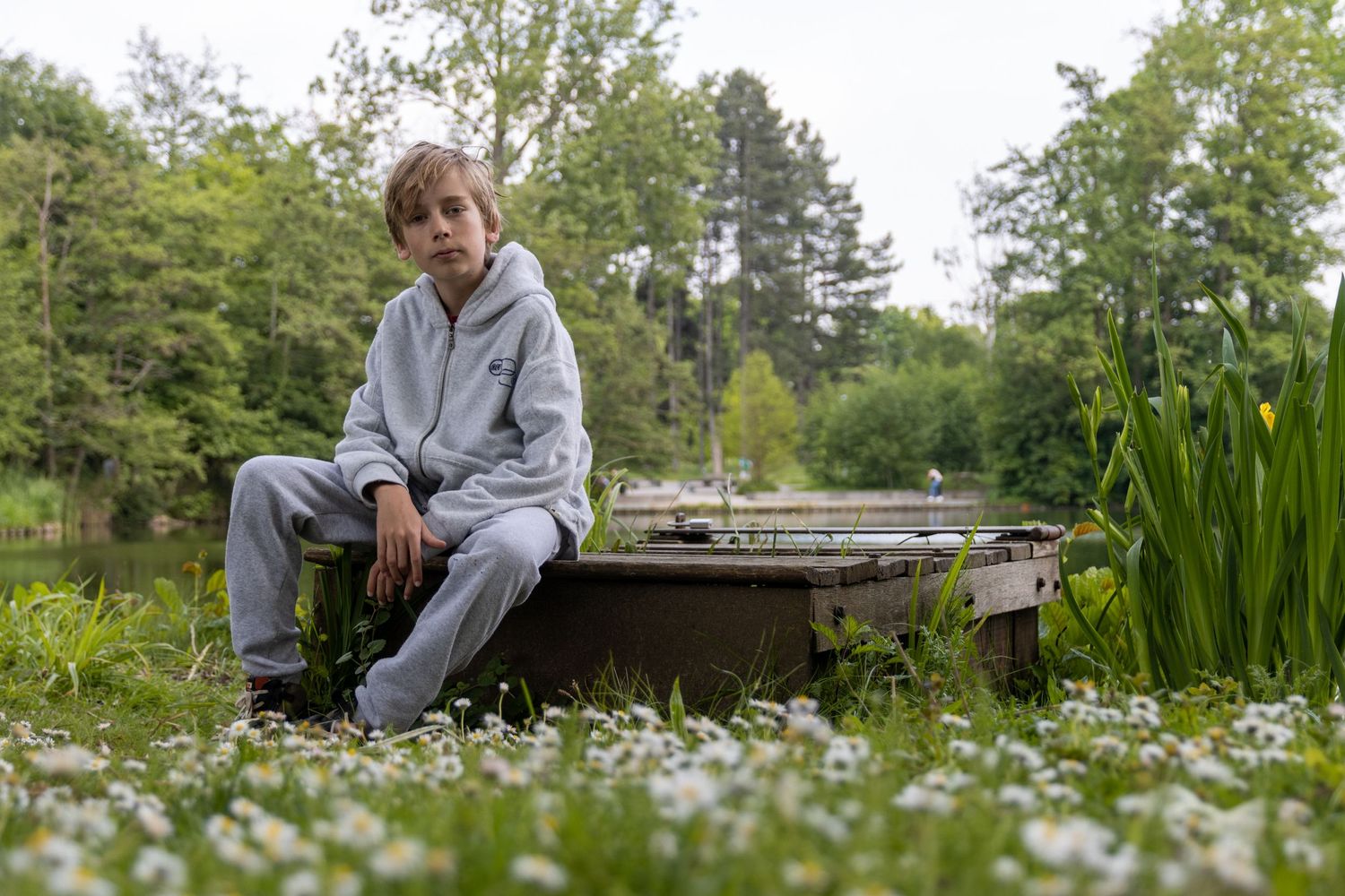 communiefoto, jongen van 12 jaar. Blonde haren. grijze broek en trui. Madeliefjes in de voorgrond. Provinciaal domein Kessel-lo