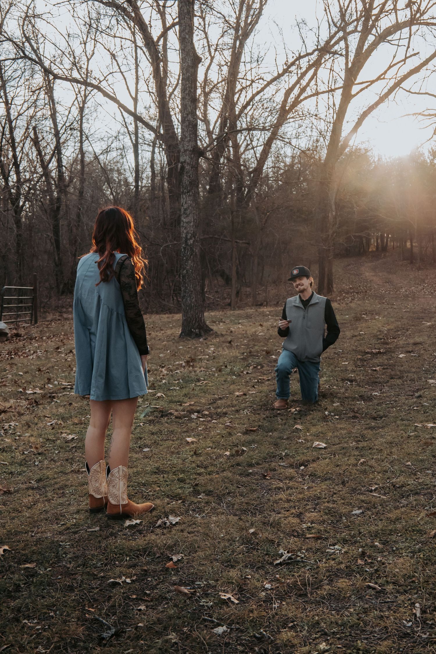 A romantic marriage proposal scene in a wooded area during golden hour sunset with autumn leaves on the ground.