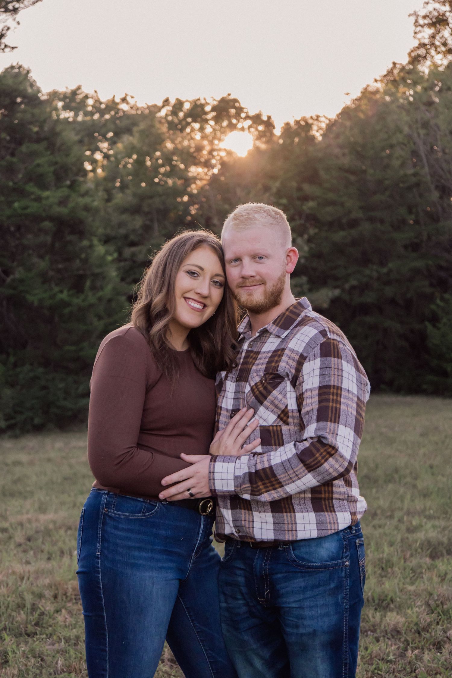 Couple in plaid and denim share intimate moment in field at sunset.