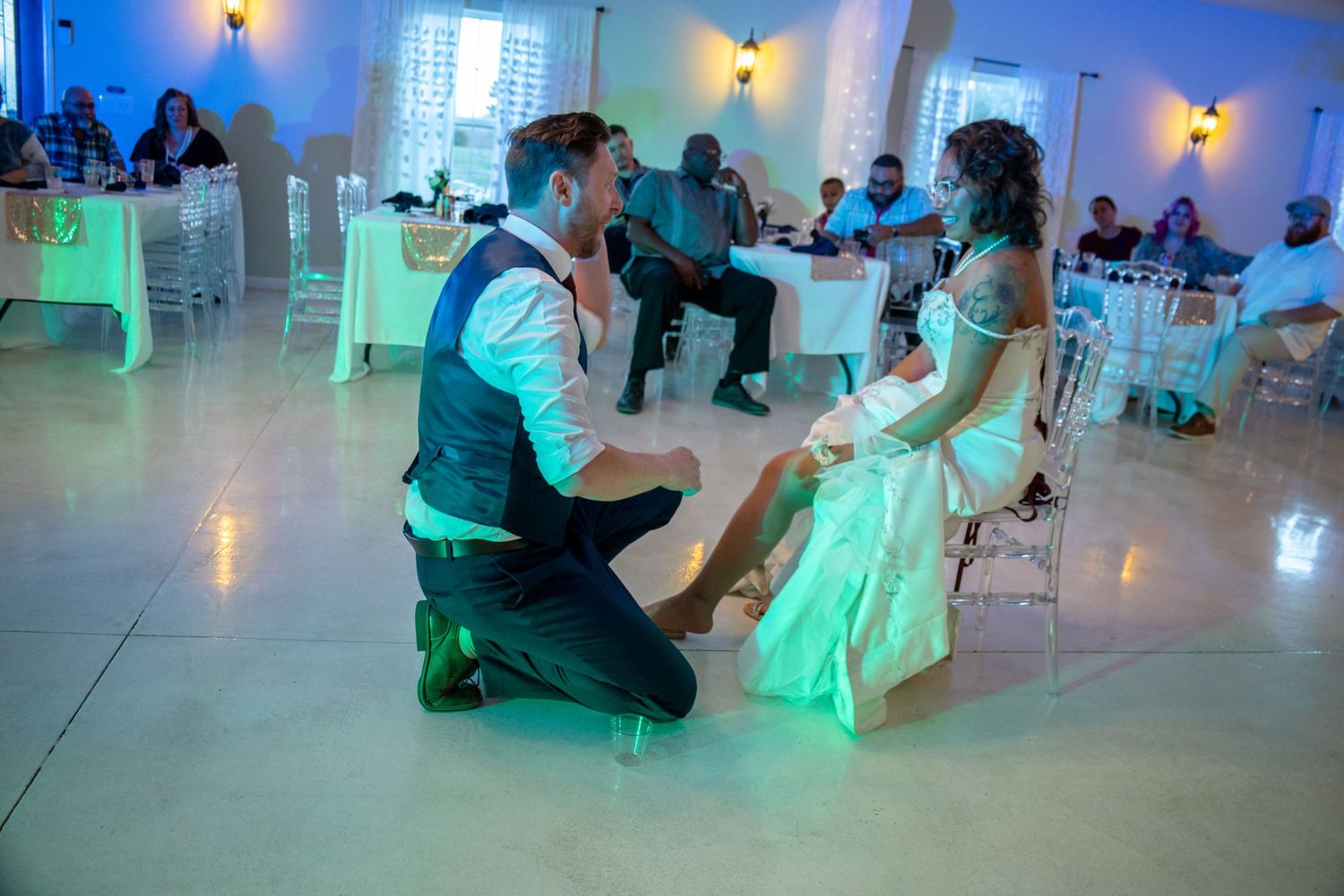 A couple shares an intimate moment during a wedding reception as neon green lights illuminate the dance floor and white decor.