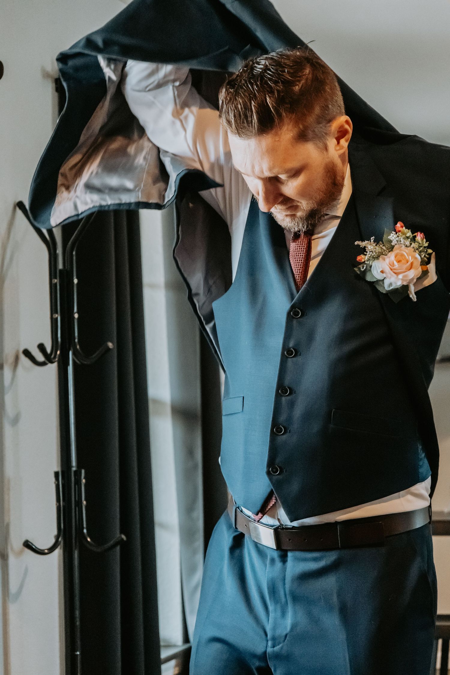 Groom in blue suit and floral boutonniere adjusts his outfit while getting ready.