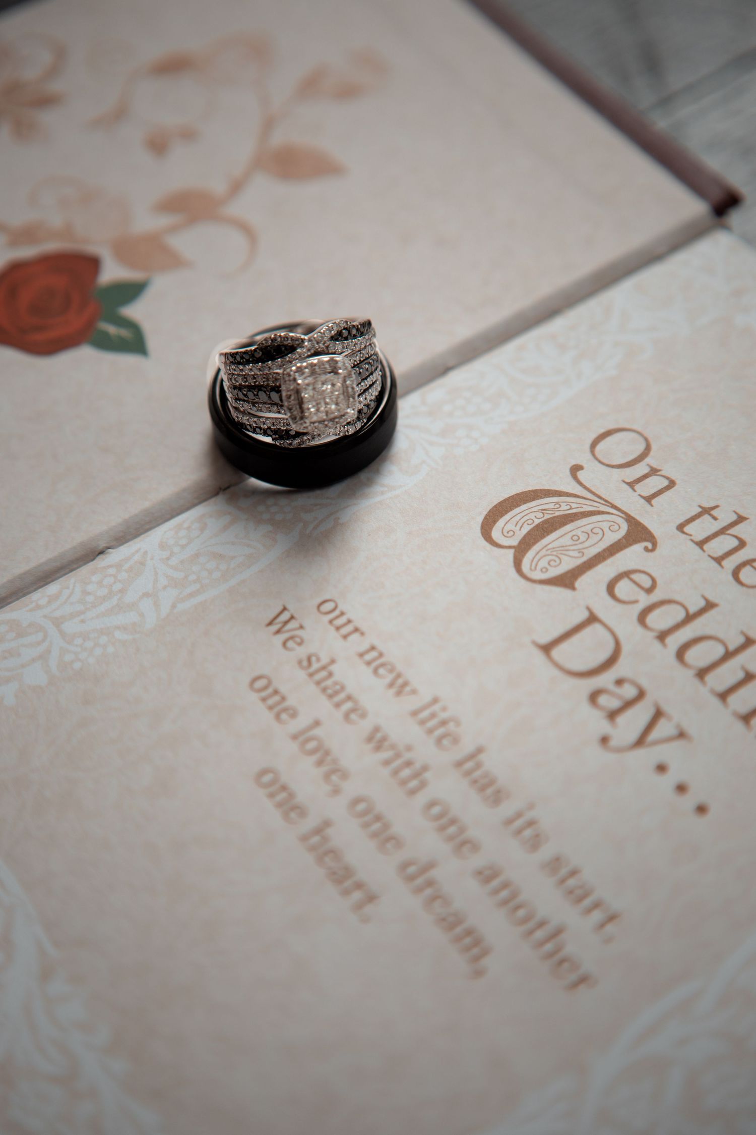 Wedding rings photographed on elegant invitation with rose gold text and floral details.