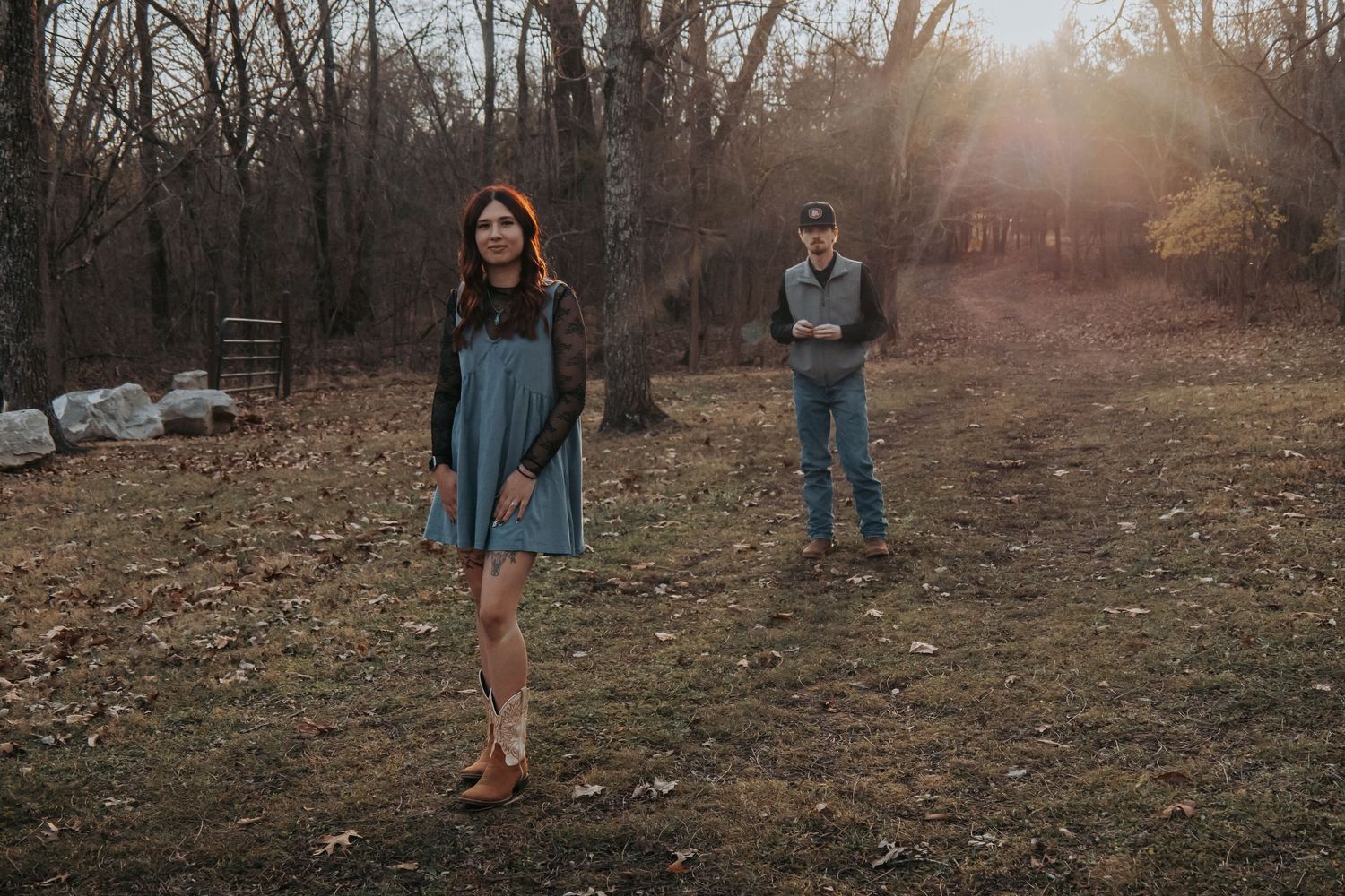 A couple poses in a wooded area during sunset for engagement photos in casual denim outfits.