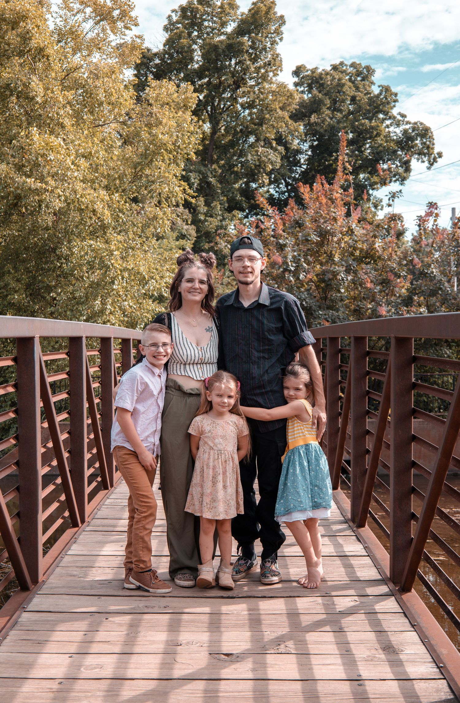 Family group photo taken on a wooden bridge walkway with trees and blue sky in the background.