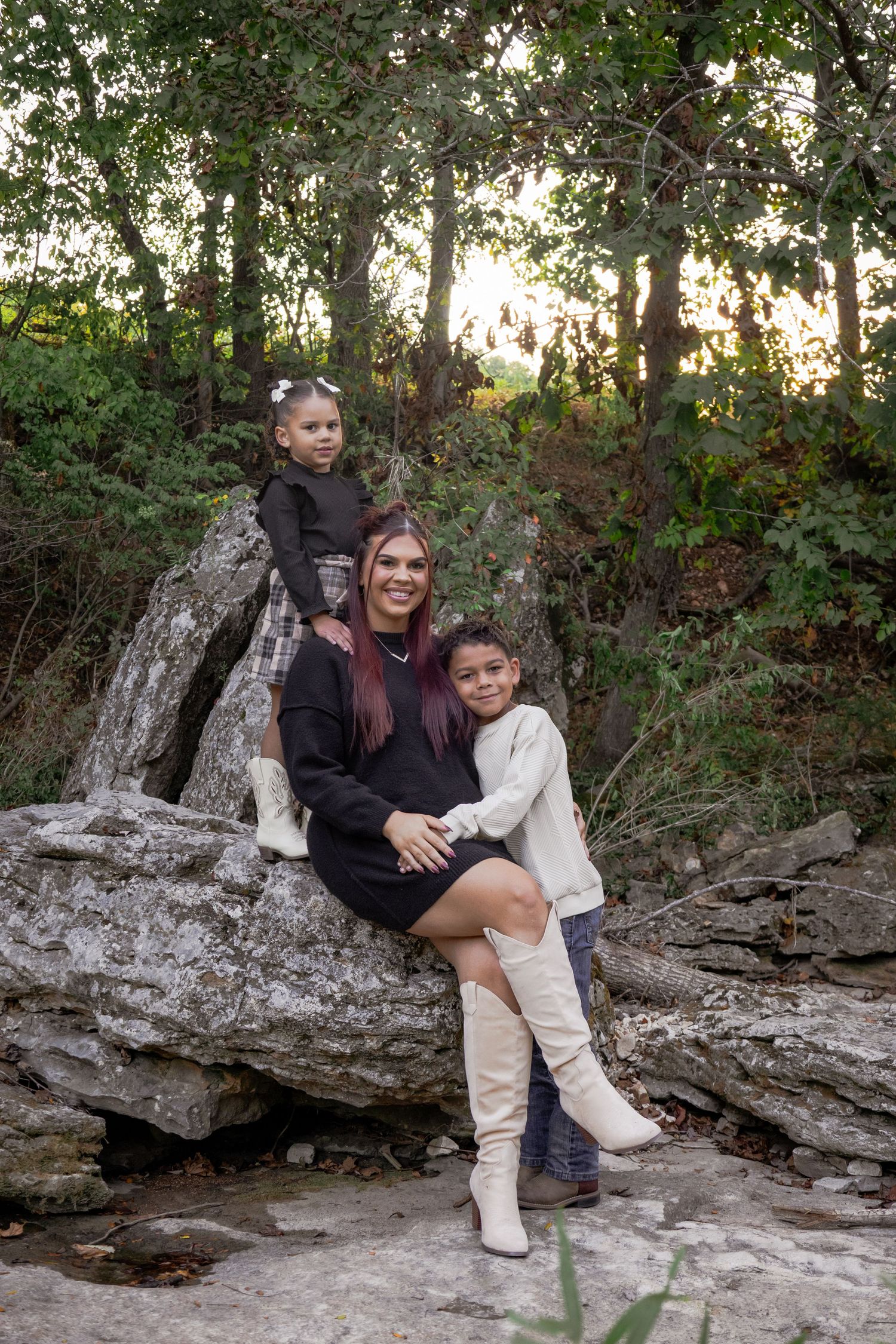 People sitting together on a rocky outcrop in a wooded natural setting during golden hour.