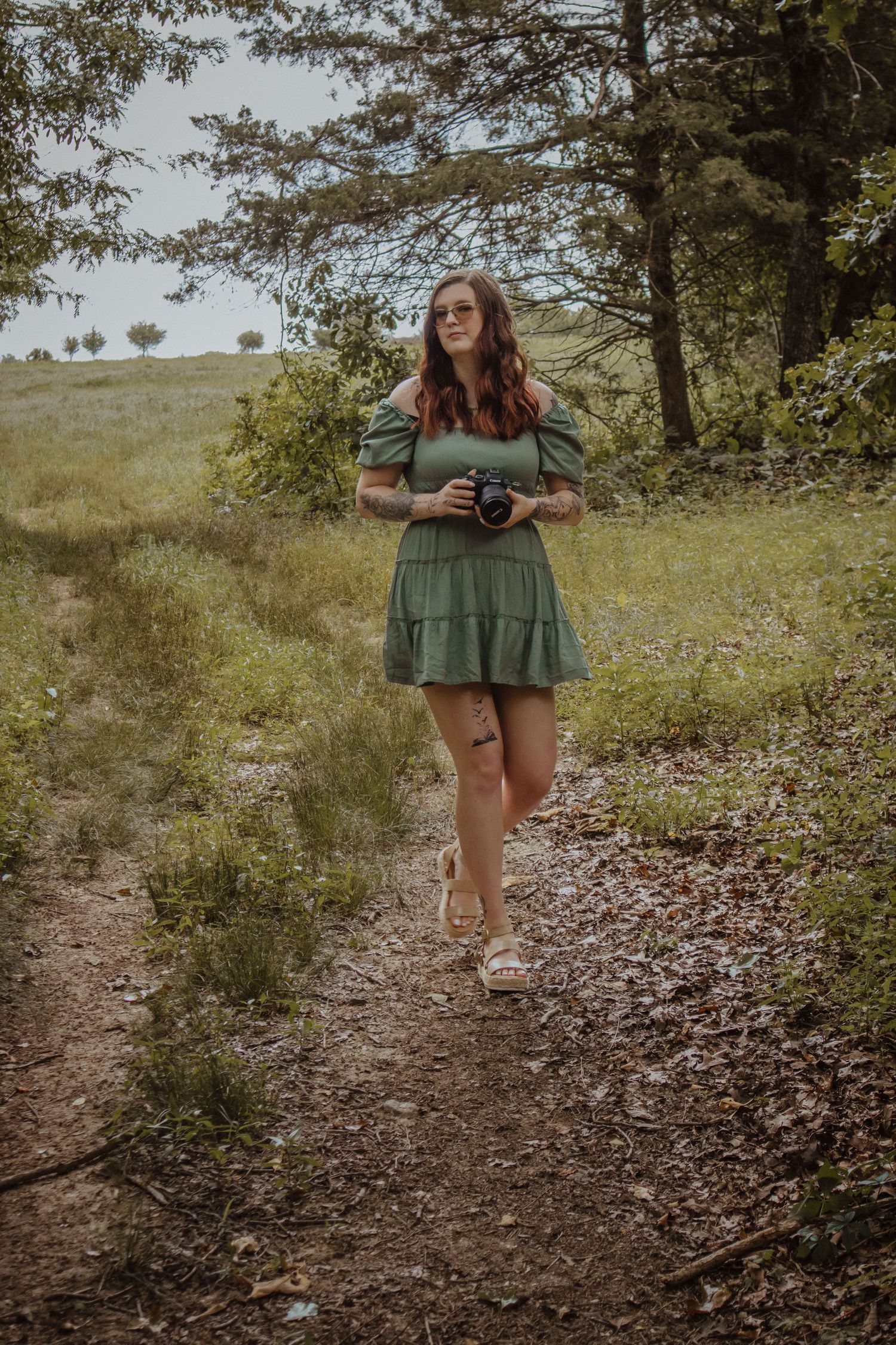 A person in a green dress twirls playfully on a dirt path surrounded by wildflowers and trees.