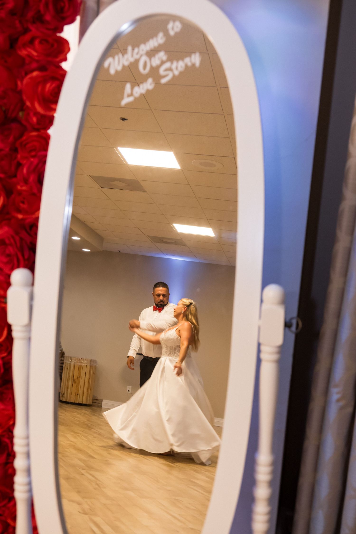 A couple dances through white archways decorated with red roses during their wedding reception.