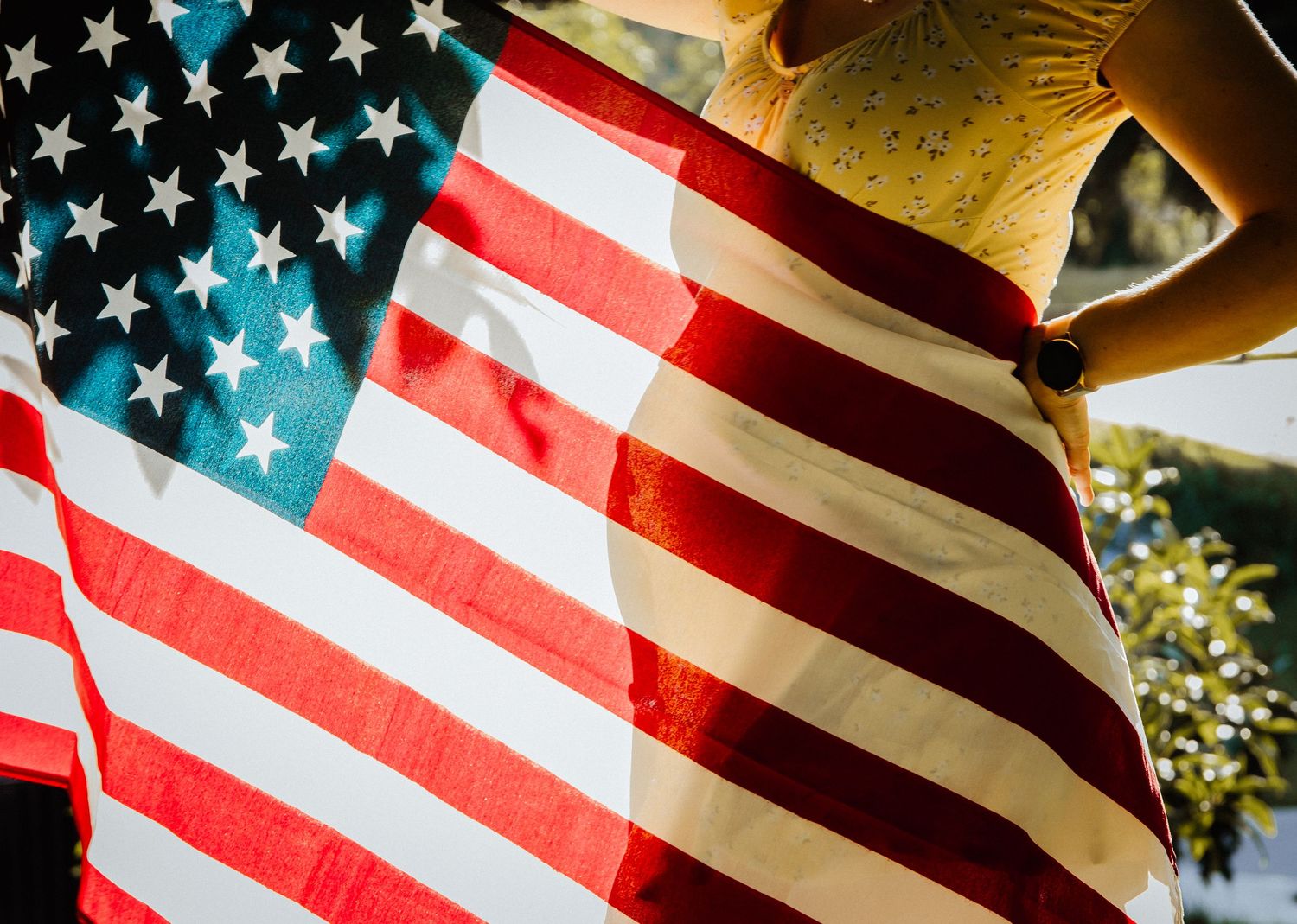 American flag with red and white stripes and stars waving in sunlight with golden glow in background.