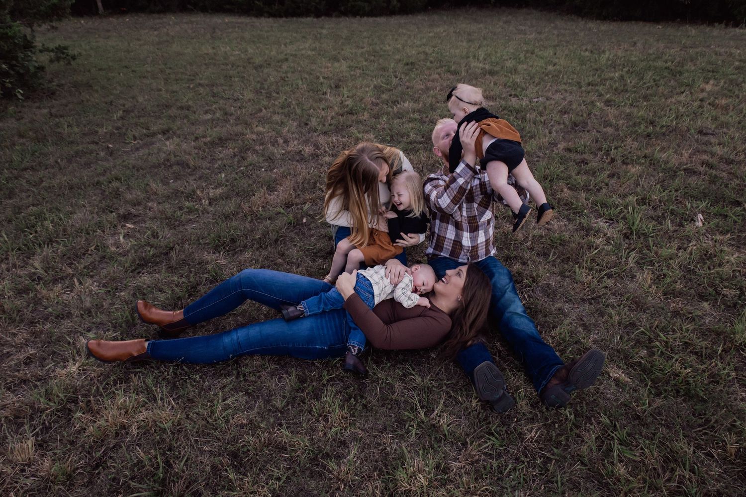 Family relaxing together on grassy field during golden hour sunset in autumn.