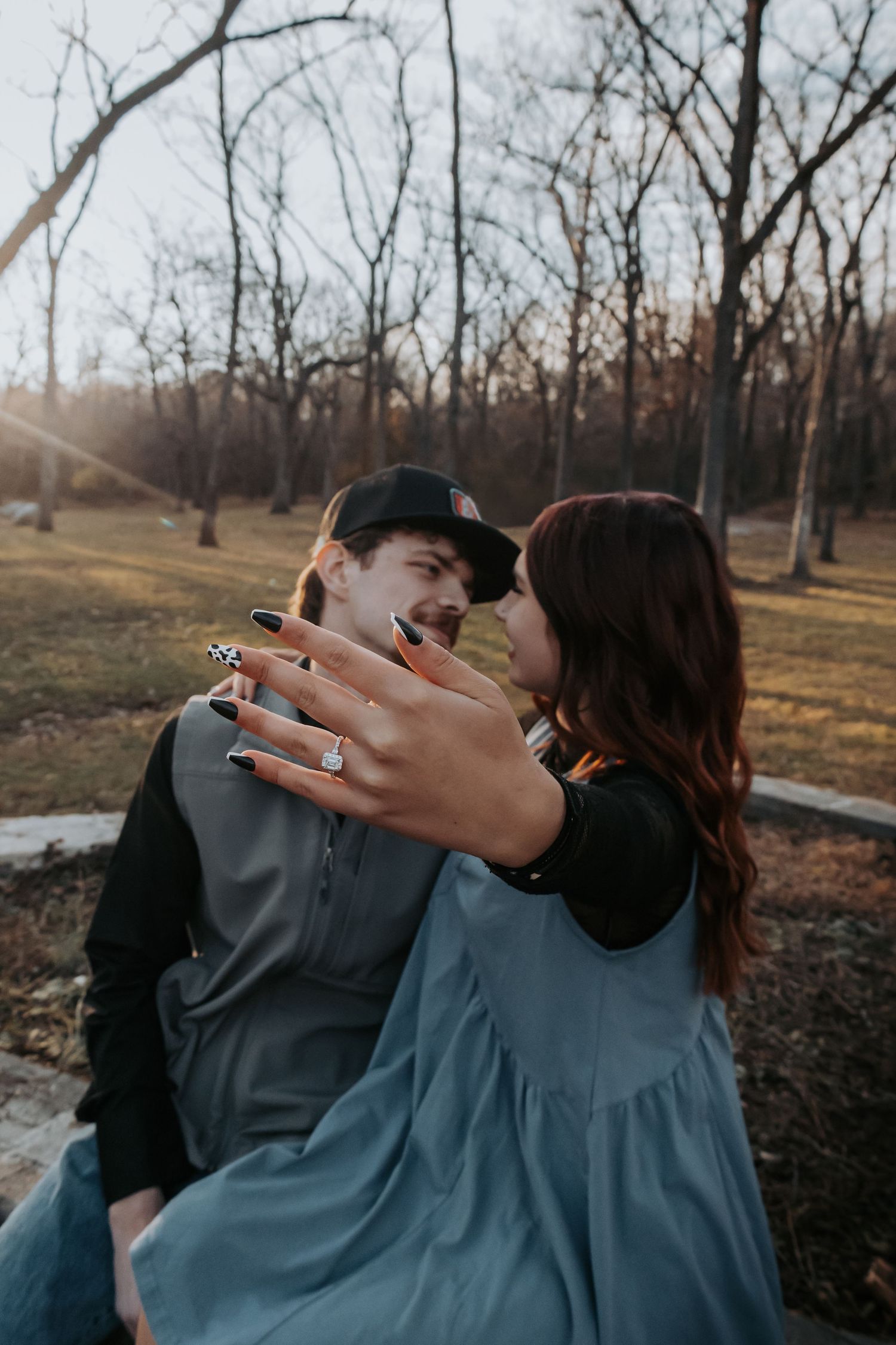 A couple in matching blue outfits embrace and kiss in a wooded outdoor setting during golden hour.