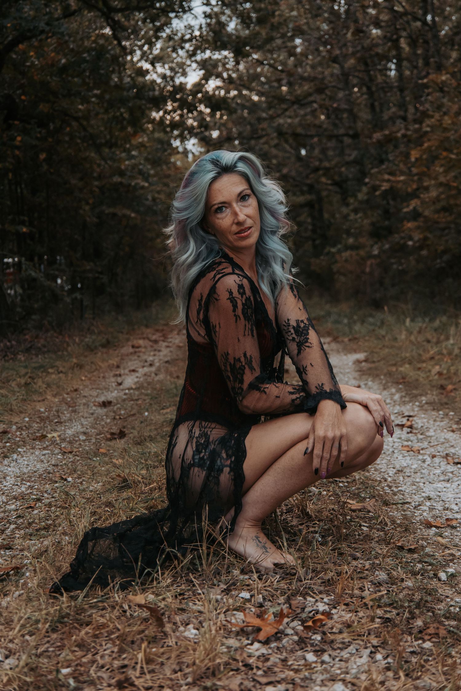 A moody autumn photoshoot in the woods with dark tones and fallen leaves on the ground.