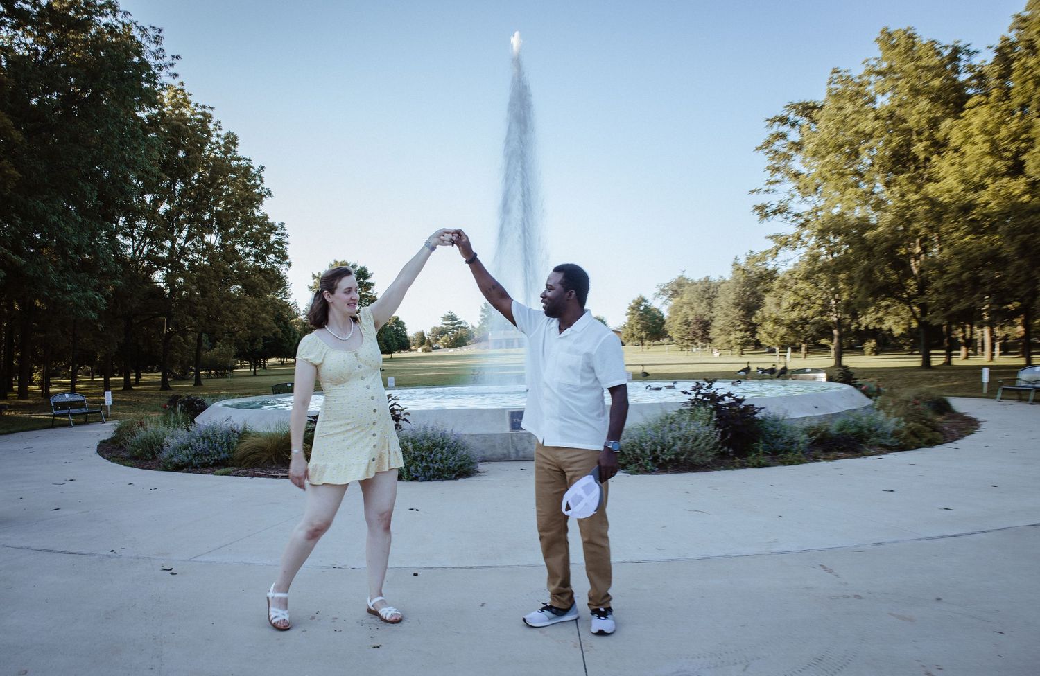 A couple walks along a scenic path holding hands with the Eiffel Tower visible in the background on a sunny day.
