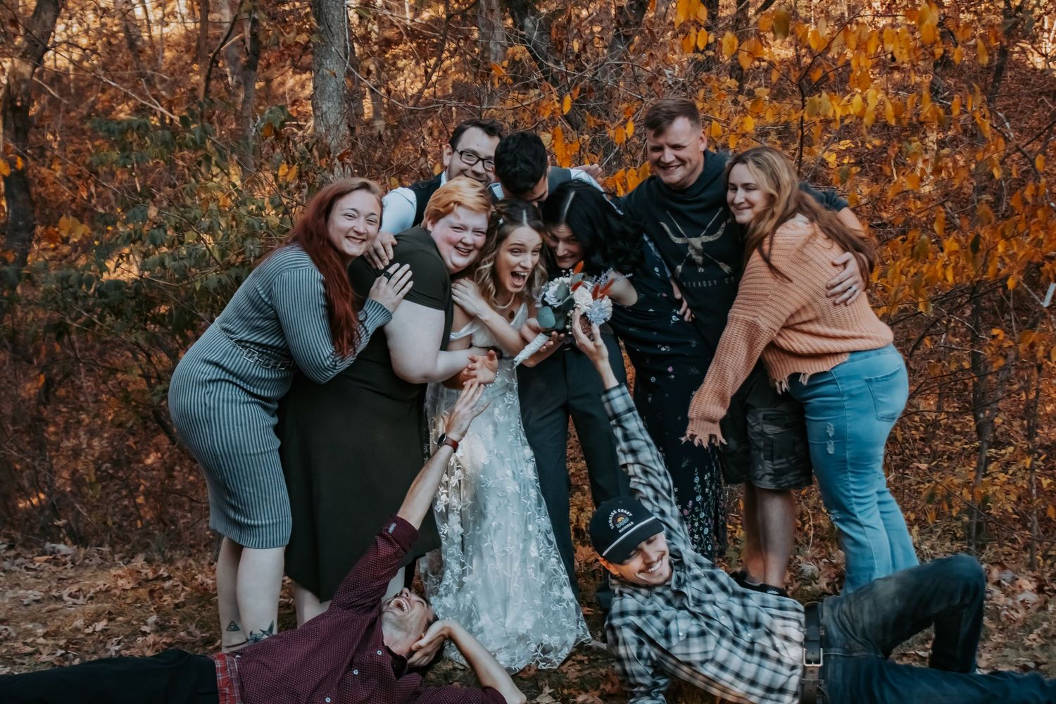 A group of people share a joyful moment together in a forest setting with vibrant autumn foliage in the background.