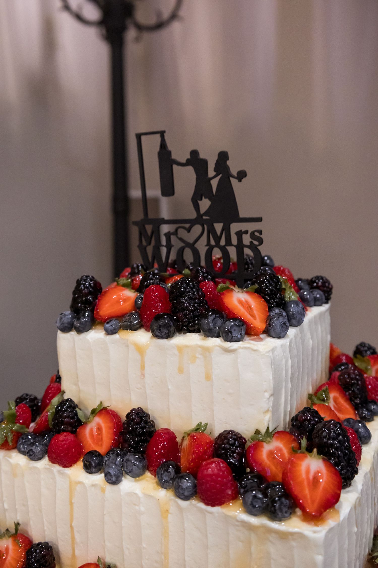 Wedding cake decorated with fresh berries and white frosting topped with a Mr & Mrs cake topper.