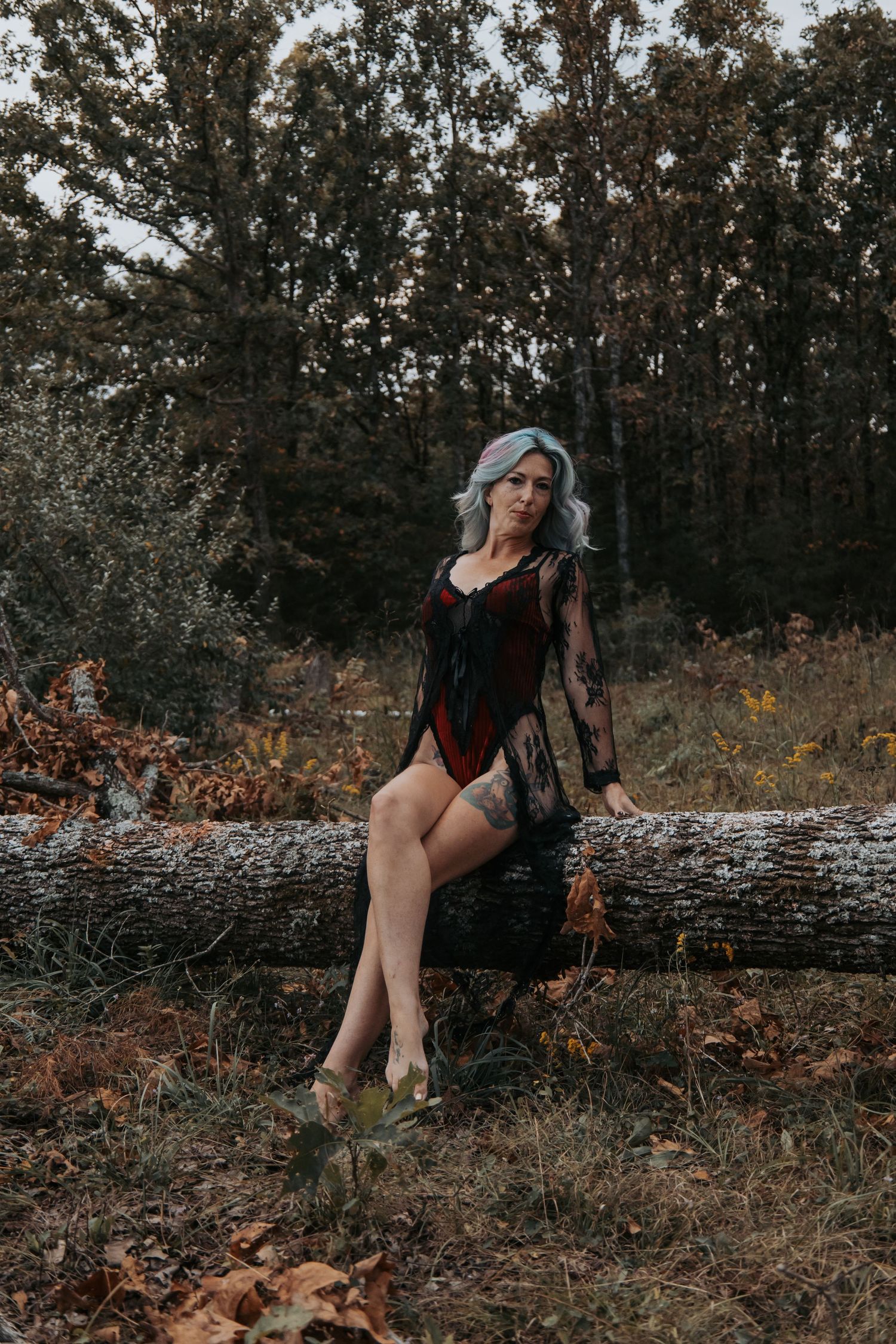 Artistic autumn photoshoot on fallen logs in a moody forest setting with muted earth tones.