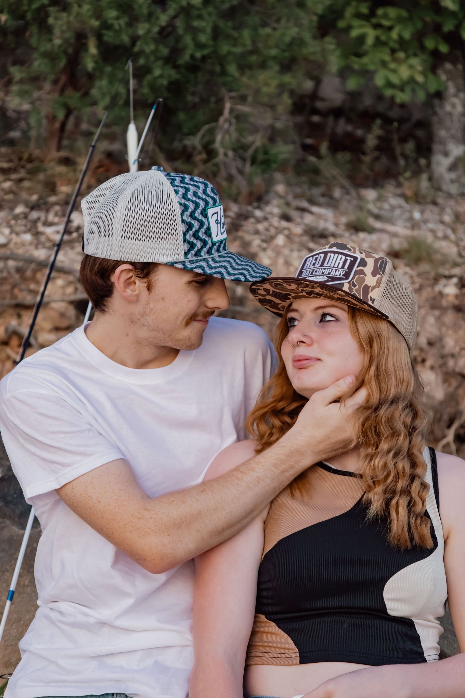 A couple shares a tender moment outdoors while wearing casual attire and baseball caps.