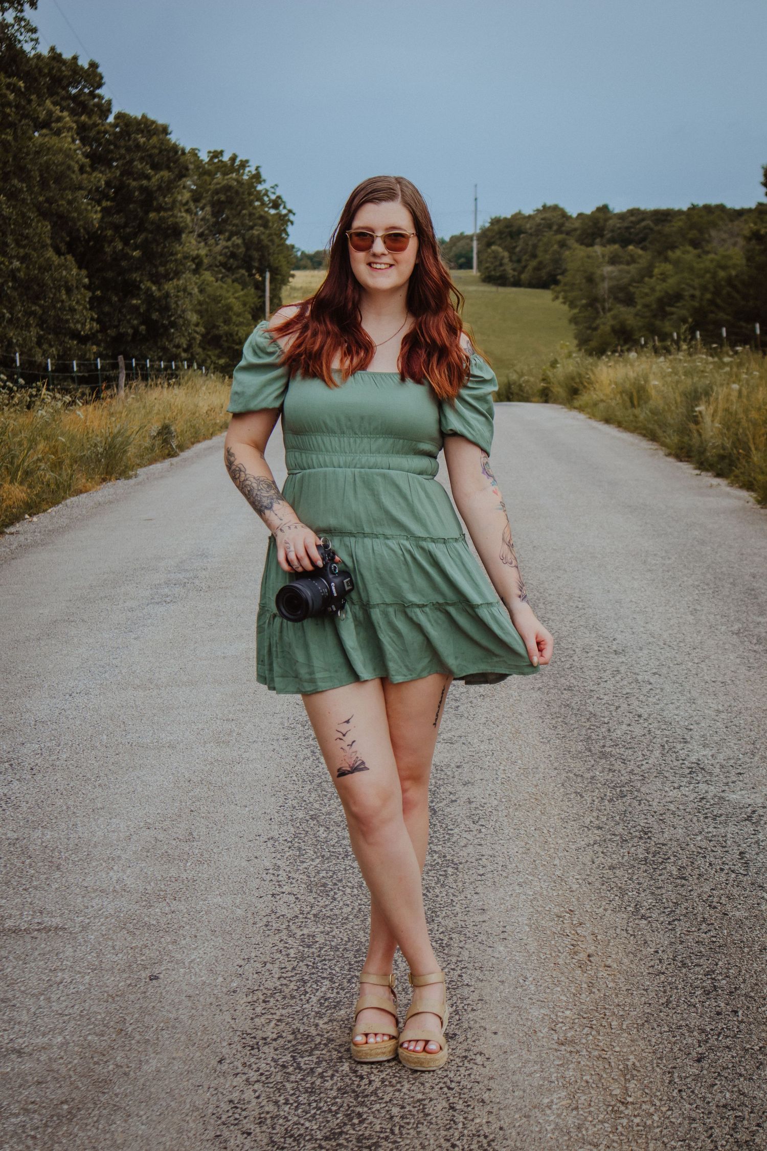 A person in a green dress poses playfully on a gravel country road on a sunny summer day.