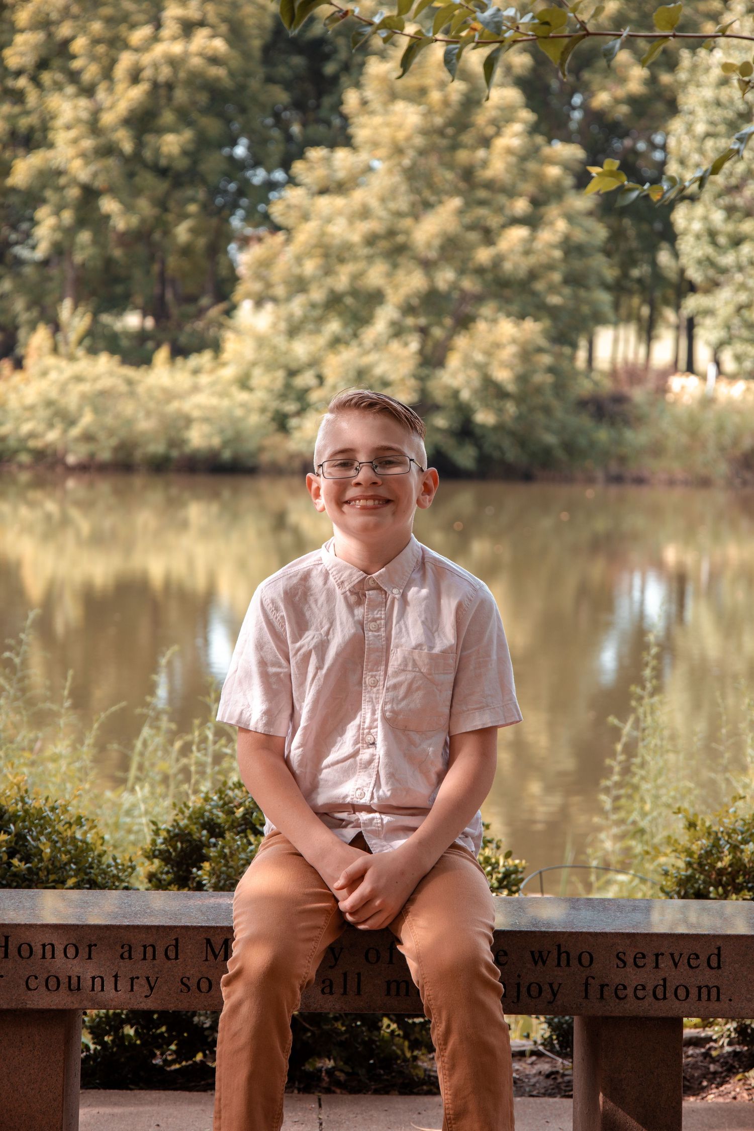 Young person sitting on a memorial bench near a serene lake with autumn trees in the background.