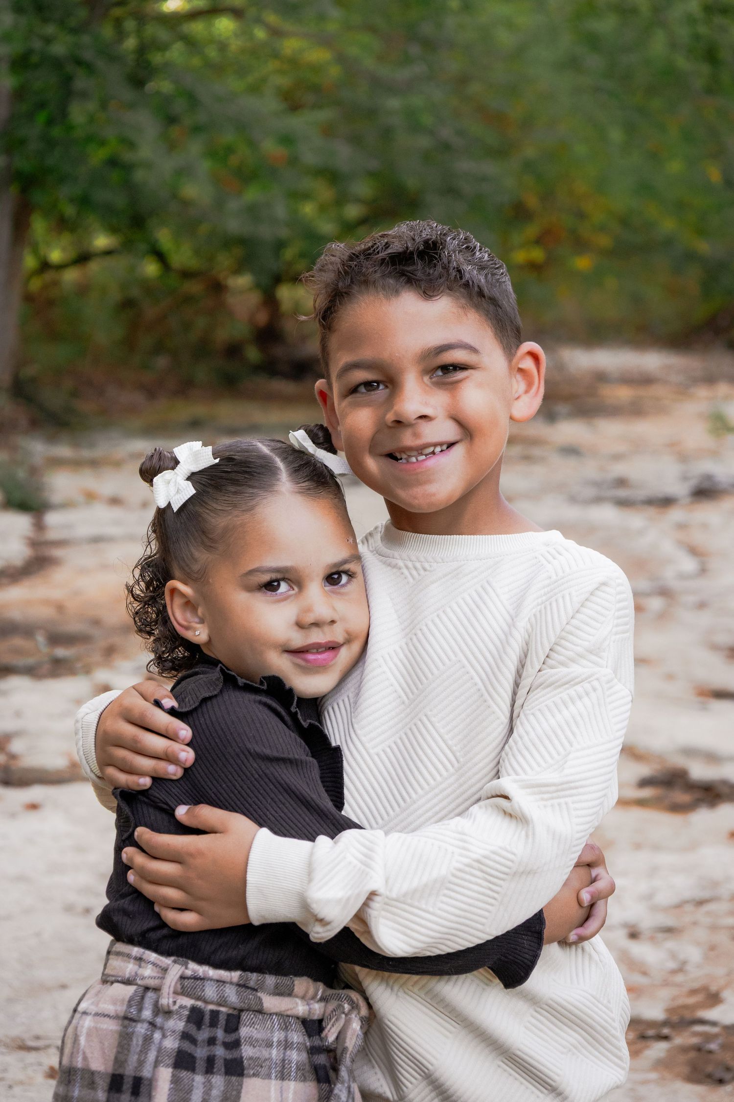 Two young children embrace warmly while wearing casual clothing outdoors in an autumn setting.