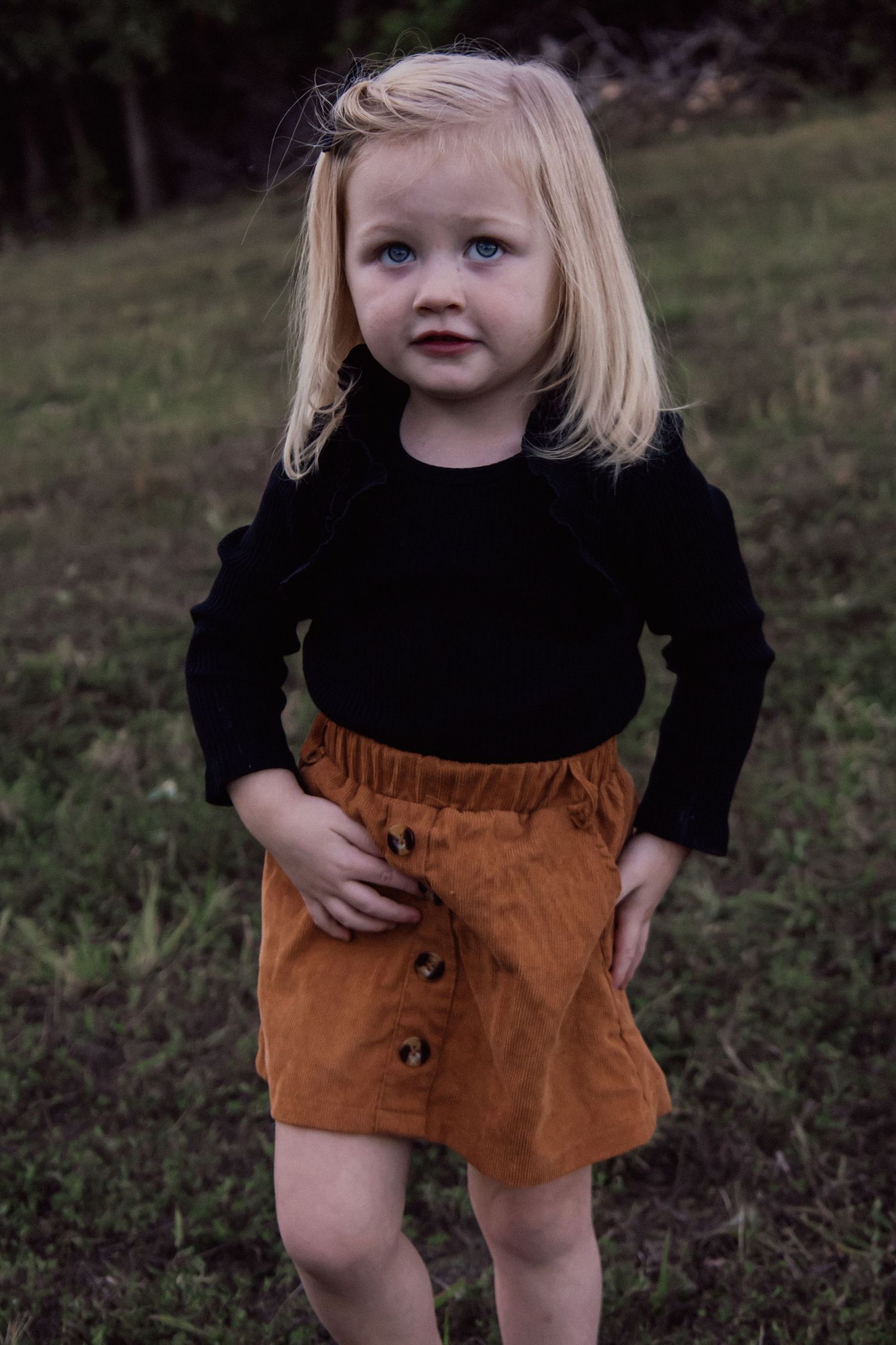 Small child wearing a black long sleeve shirt and brown corduroy shorts plays outdoors in autumn.