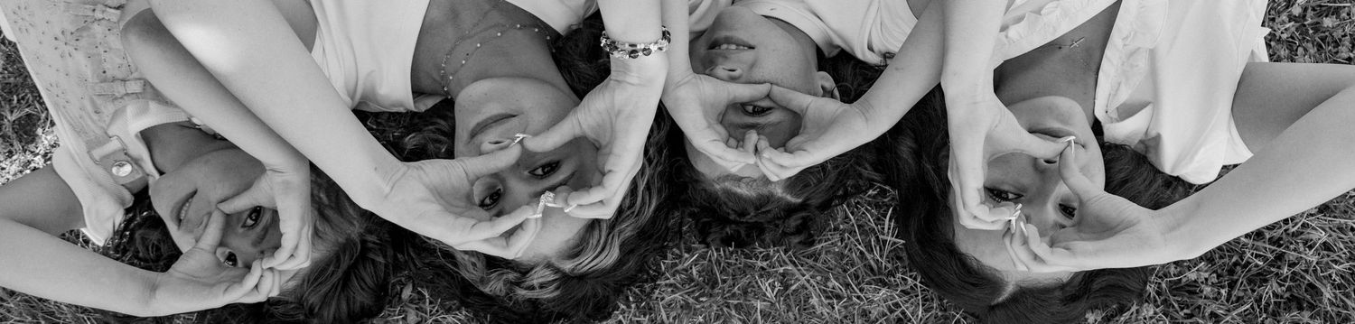 Black and white photo of bridesmaids lying on grass making heart shapes with their hands.