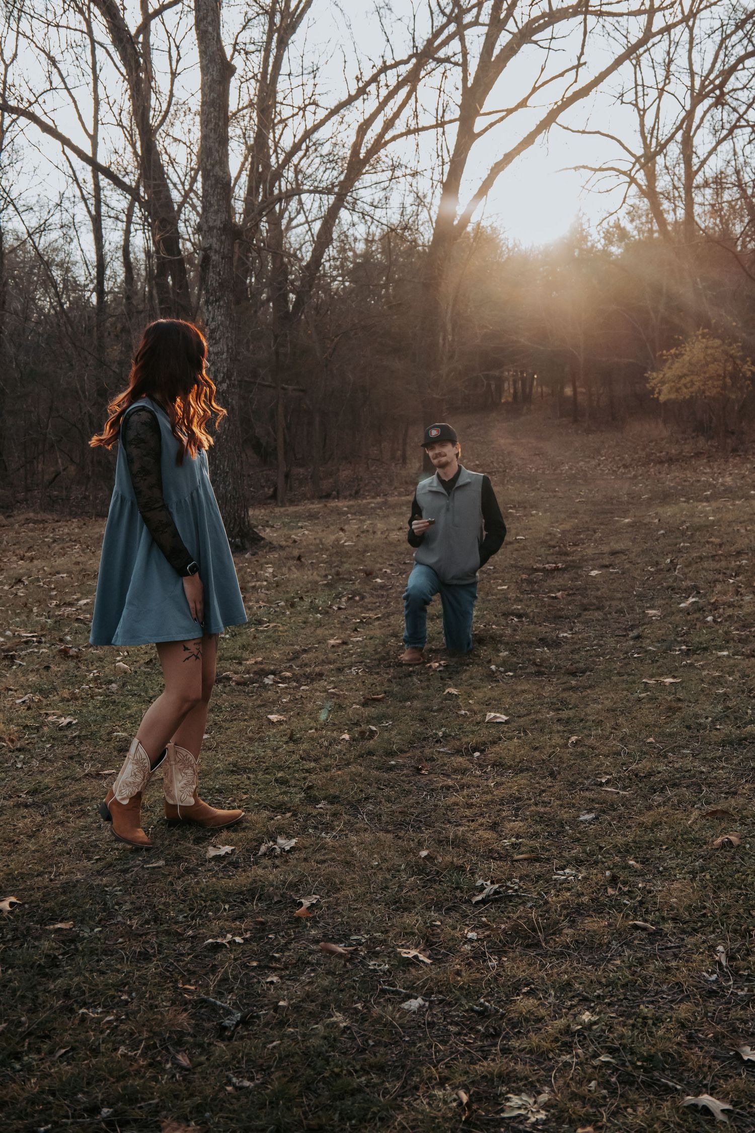 Couple enjoying a playful autumn photoshoot in a wooded area during golden hour sunset.