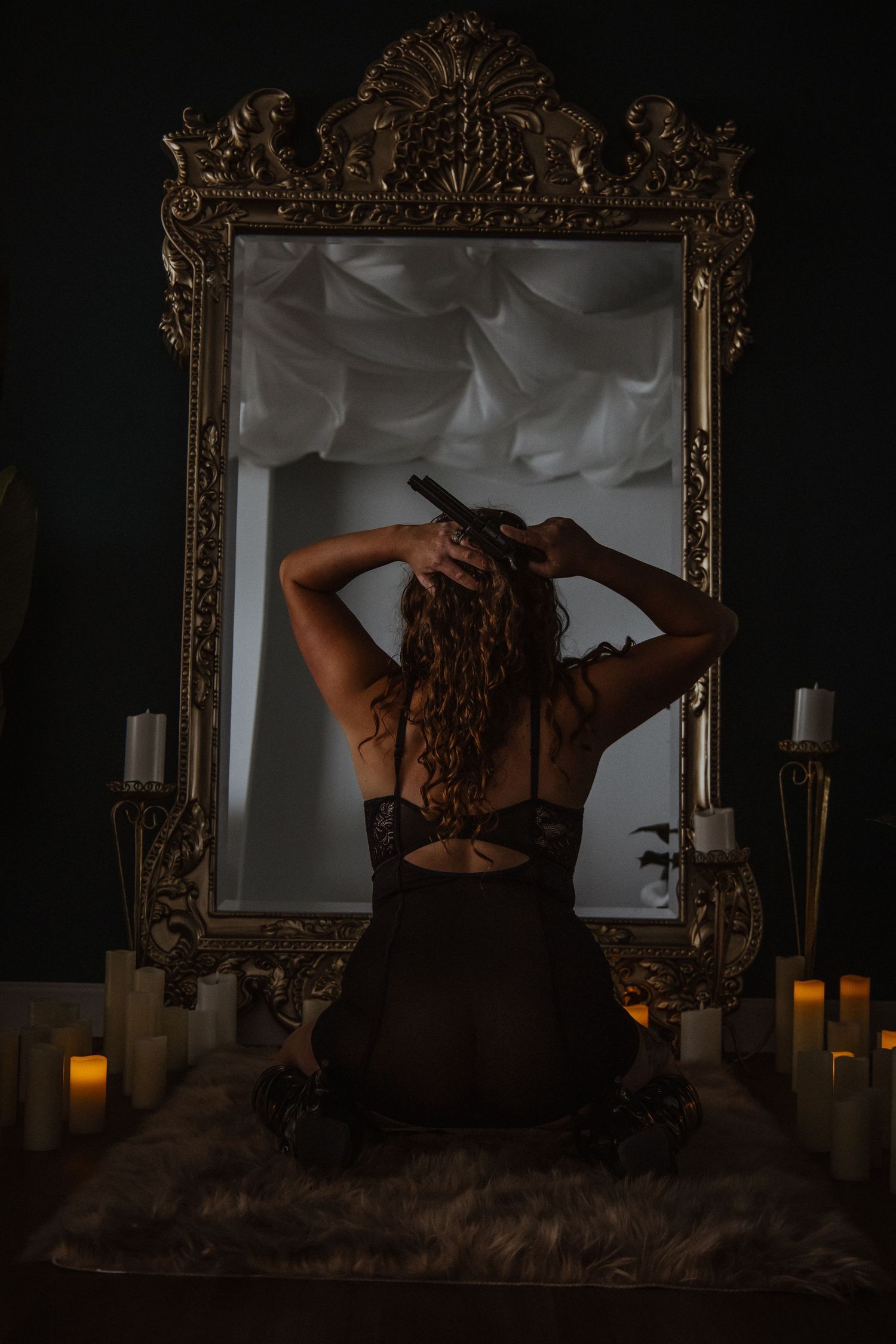 Silhouette reflected in ornate gold mirror with glowing candles creating moody boudoir atmosphere in dark room.