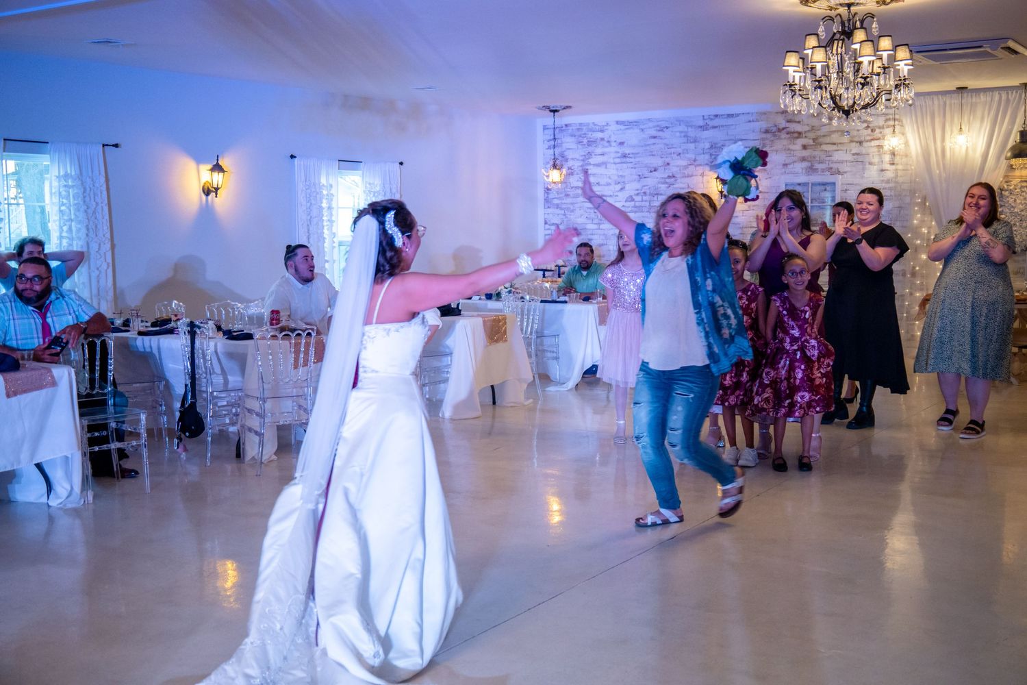 Wedding celebration with dancers on a white dance floor under elegant chandeliers in a decorated reception venue.