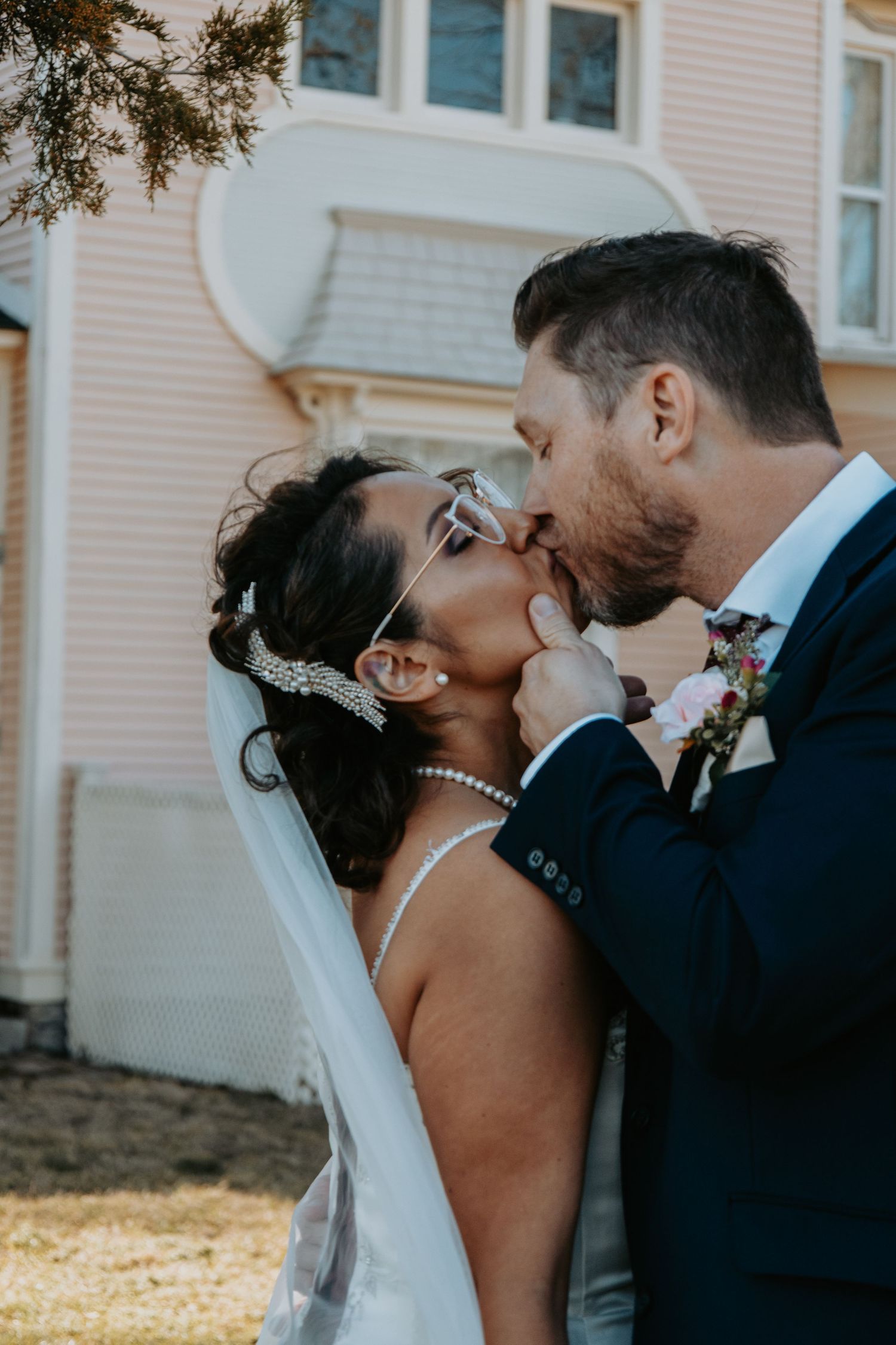 Intimate wedding moment captured outside a pink historic building on a sunny afternoon.