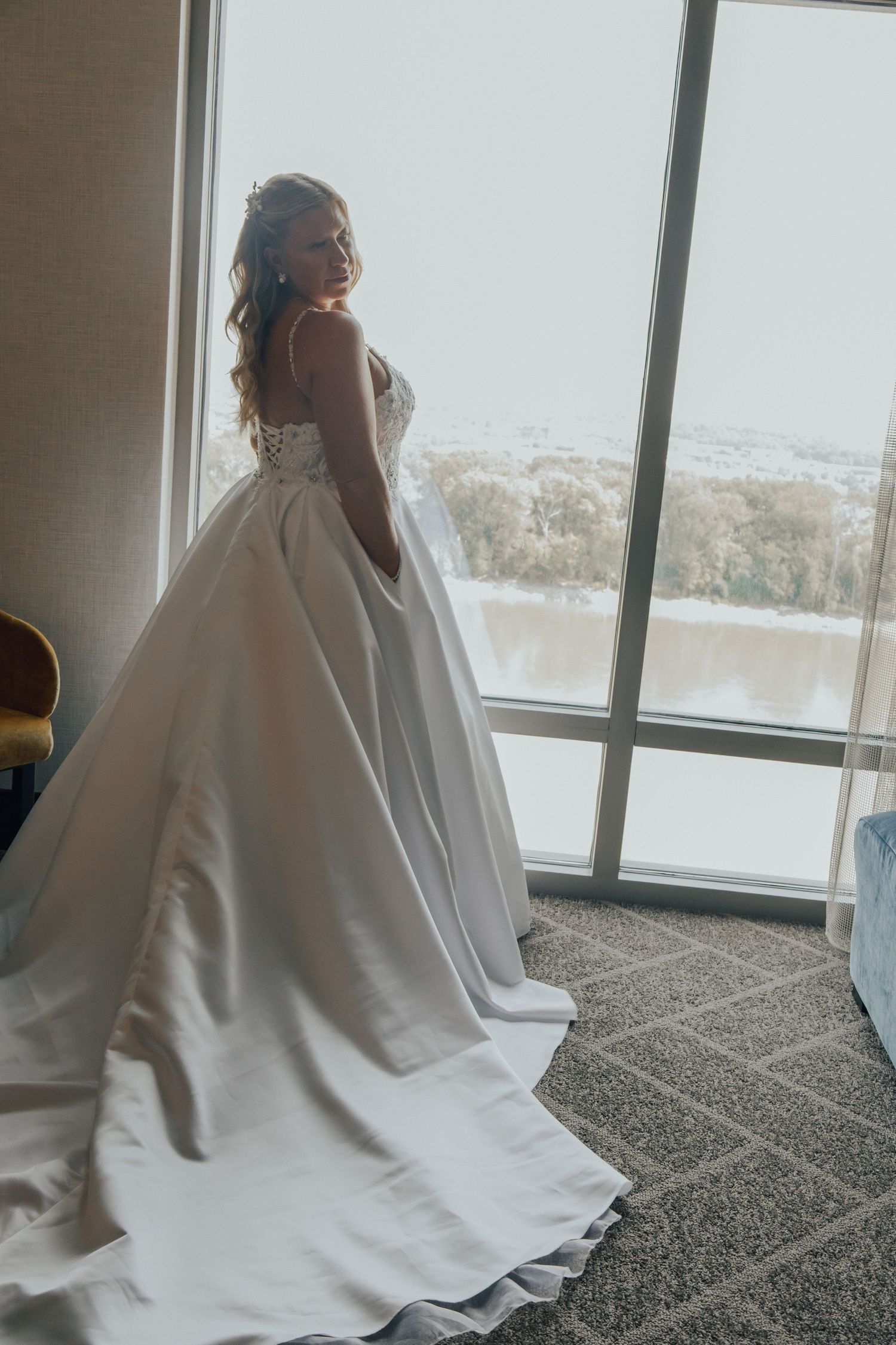 A bride in a flowing white wedding gown poses near large windows with a scenic view in a series of photos.