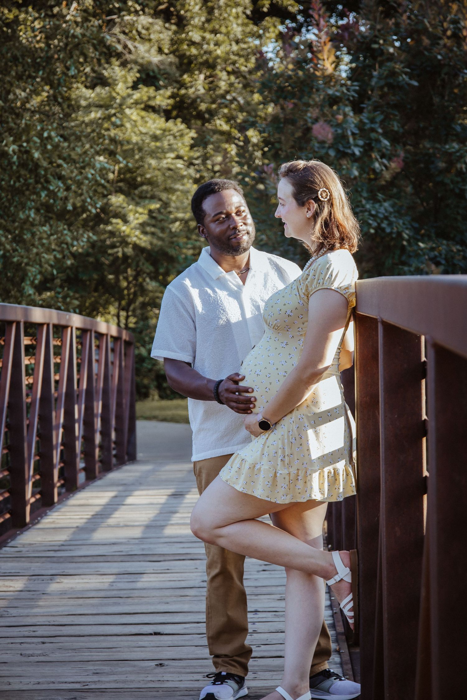 A couple shares intimate moments on a wooden bridge in a park setting during a photo session.