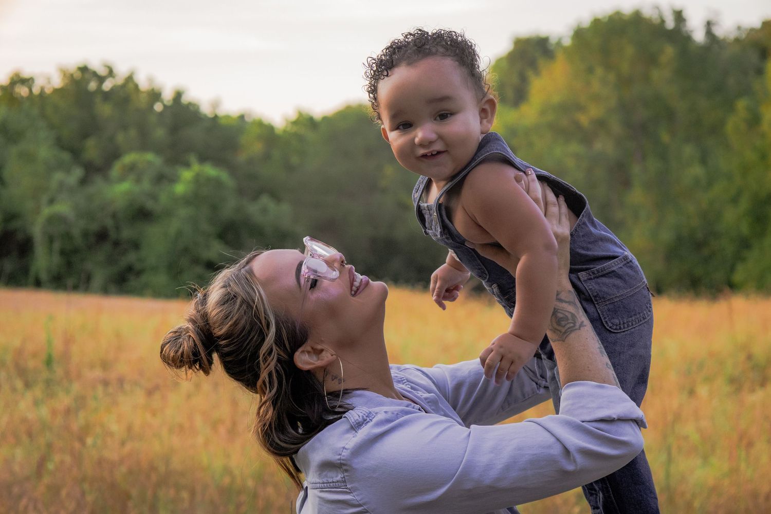 A couple shares a romantic embrace while sitting in a golden sunlit meadow during an outdoor photo session.
