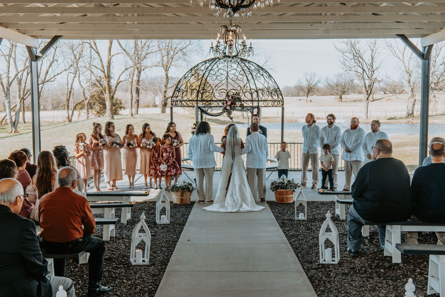 Outdoor wedding ceremony under a gazebo with attendants in coral and light blue colors standing beside a couple.