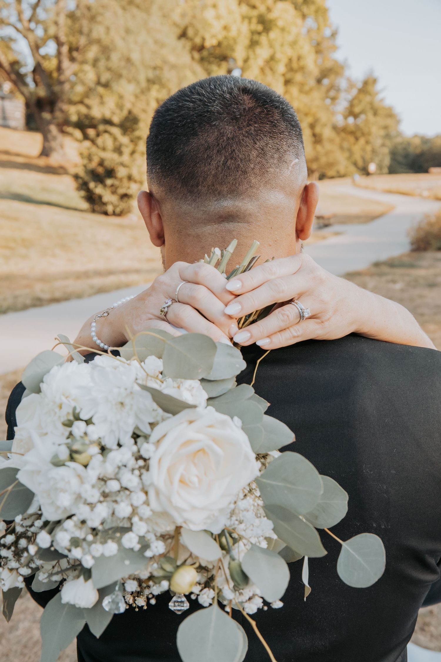 A groom in a black suit holds a romantic white and blush wedding bouquet with roses and eucalyptus leaves.