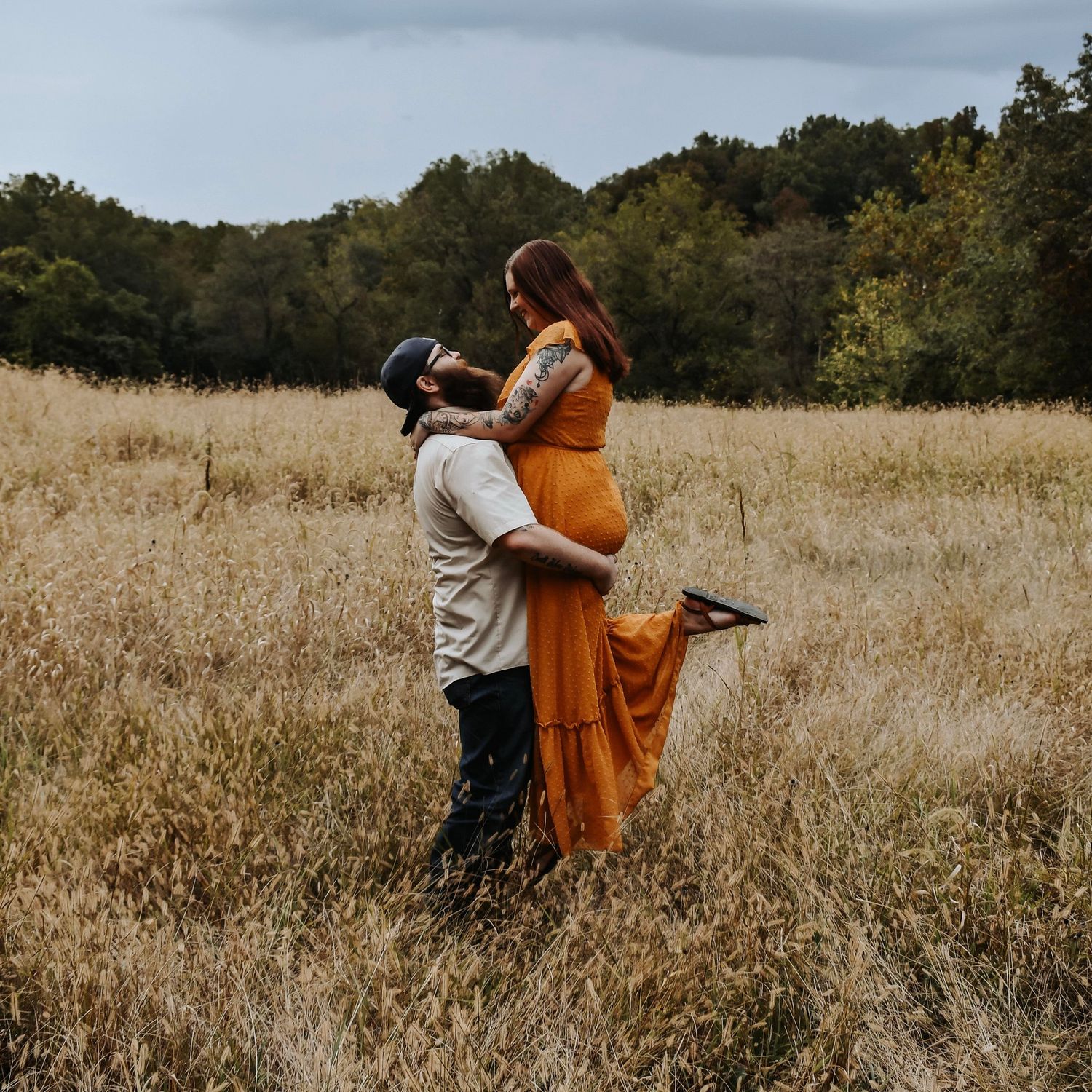 Couple dancing in a golden field of tall grass at sunset with flowing orange fabric creating graceful movement.