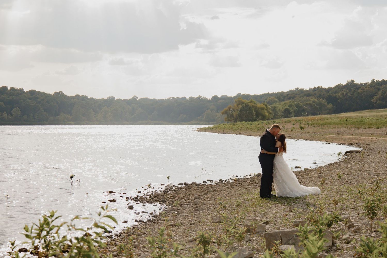A foggy lakeside wedding ceremony with guests seated along the shoreline under overcast skies.