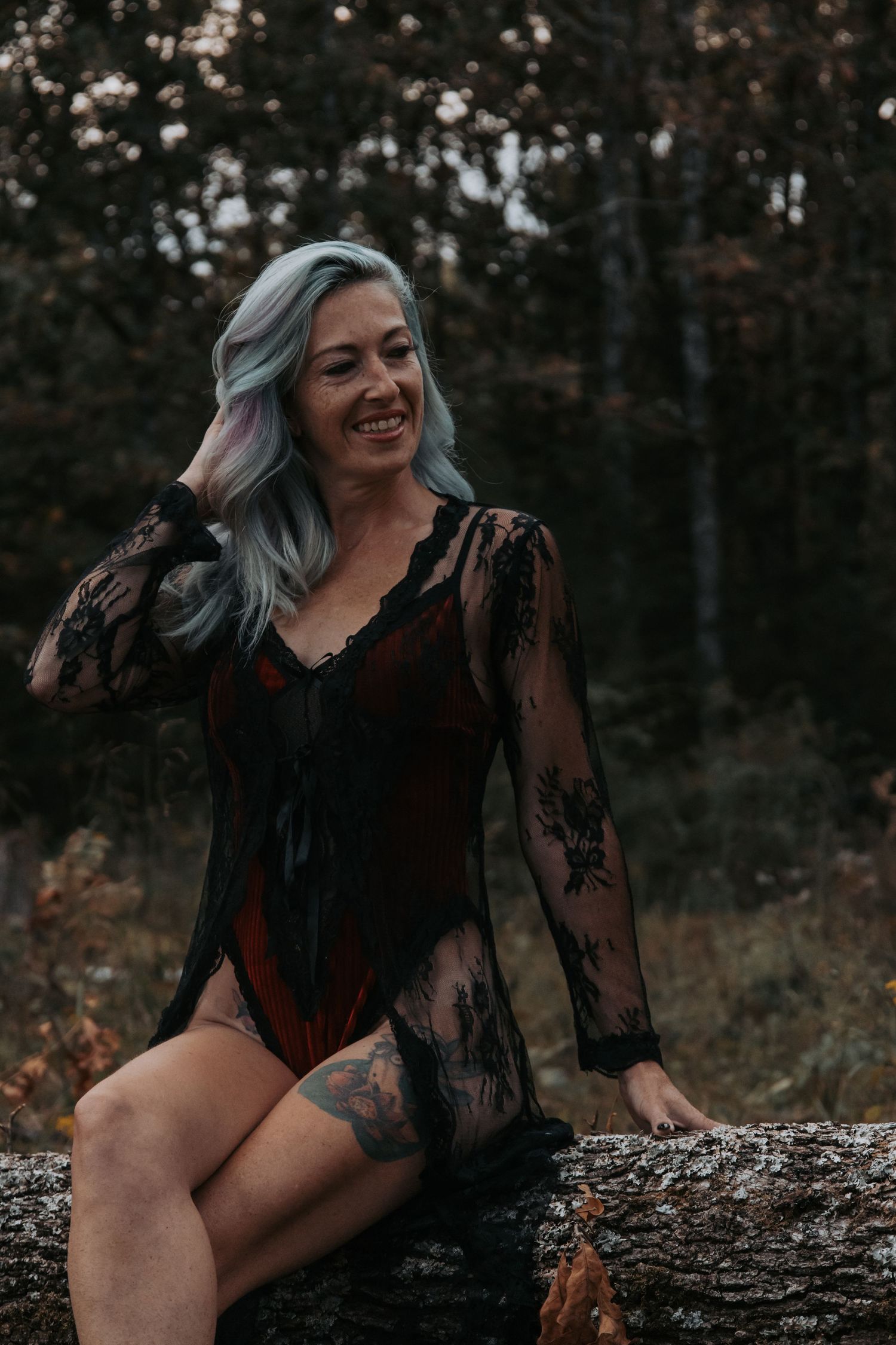 An artistic boudoir photography session on a fallen log in a dark forest setting.