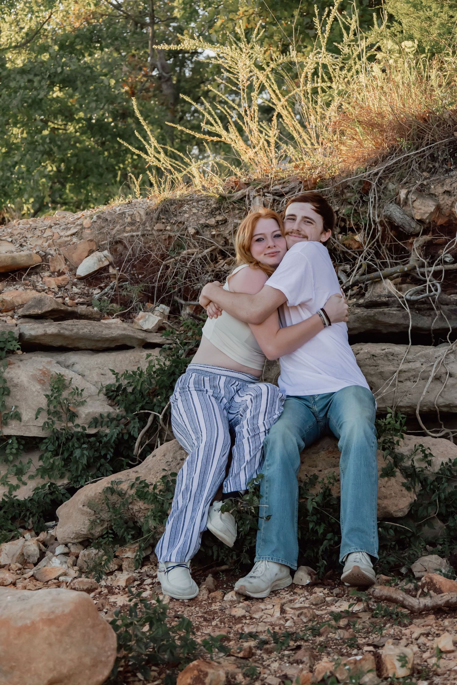 A couple sits together on a fallen log in a natural outdoor setting during golden hour lighting.