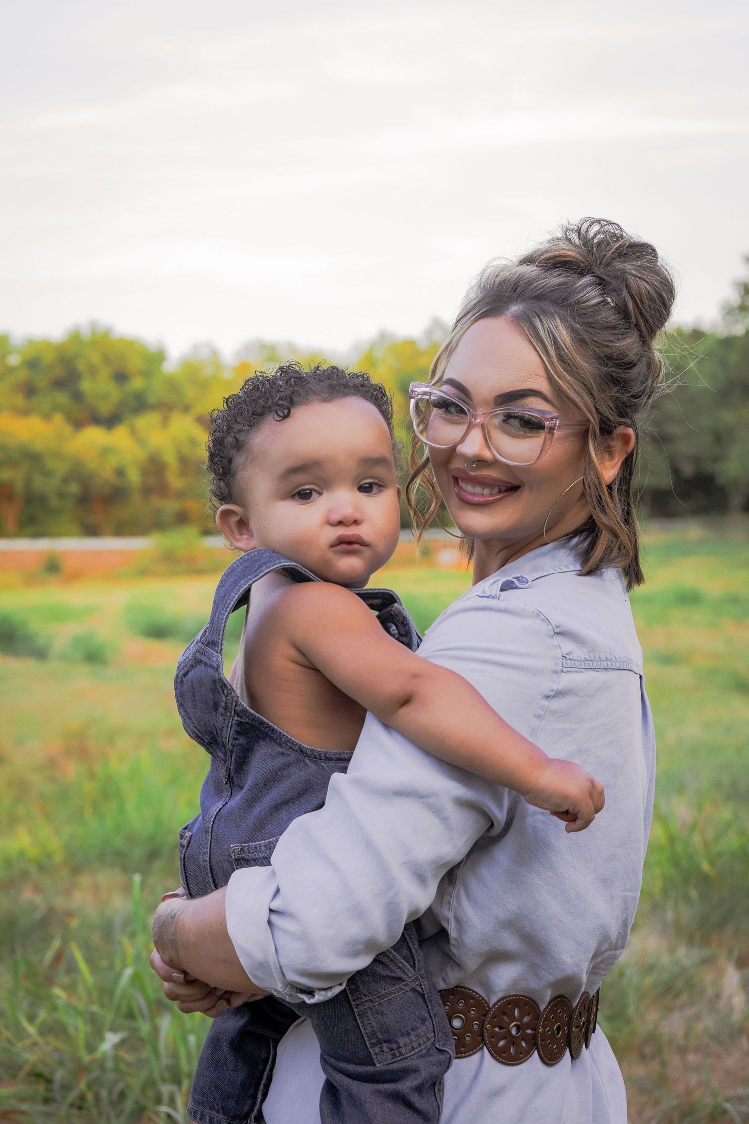 A tender outdoor photoshoot in a grassy field showing loving embraces and playful moments between parent and child.